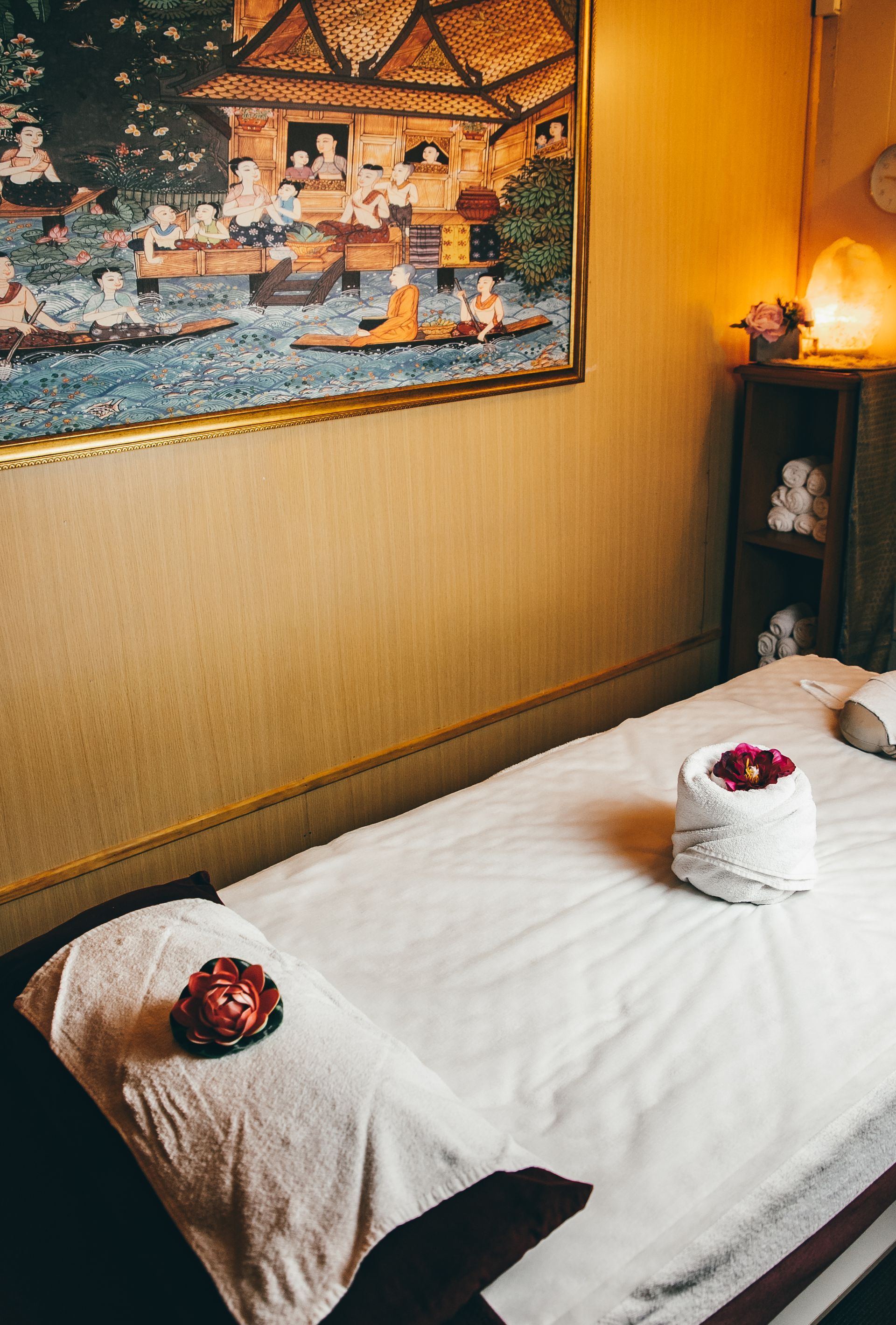 Massage table with white linens, flowers, and a painting in a spa setting.