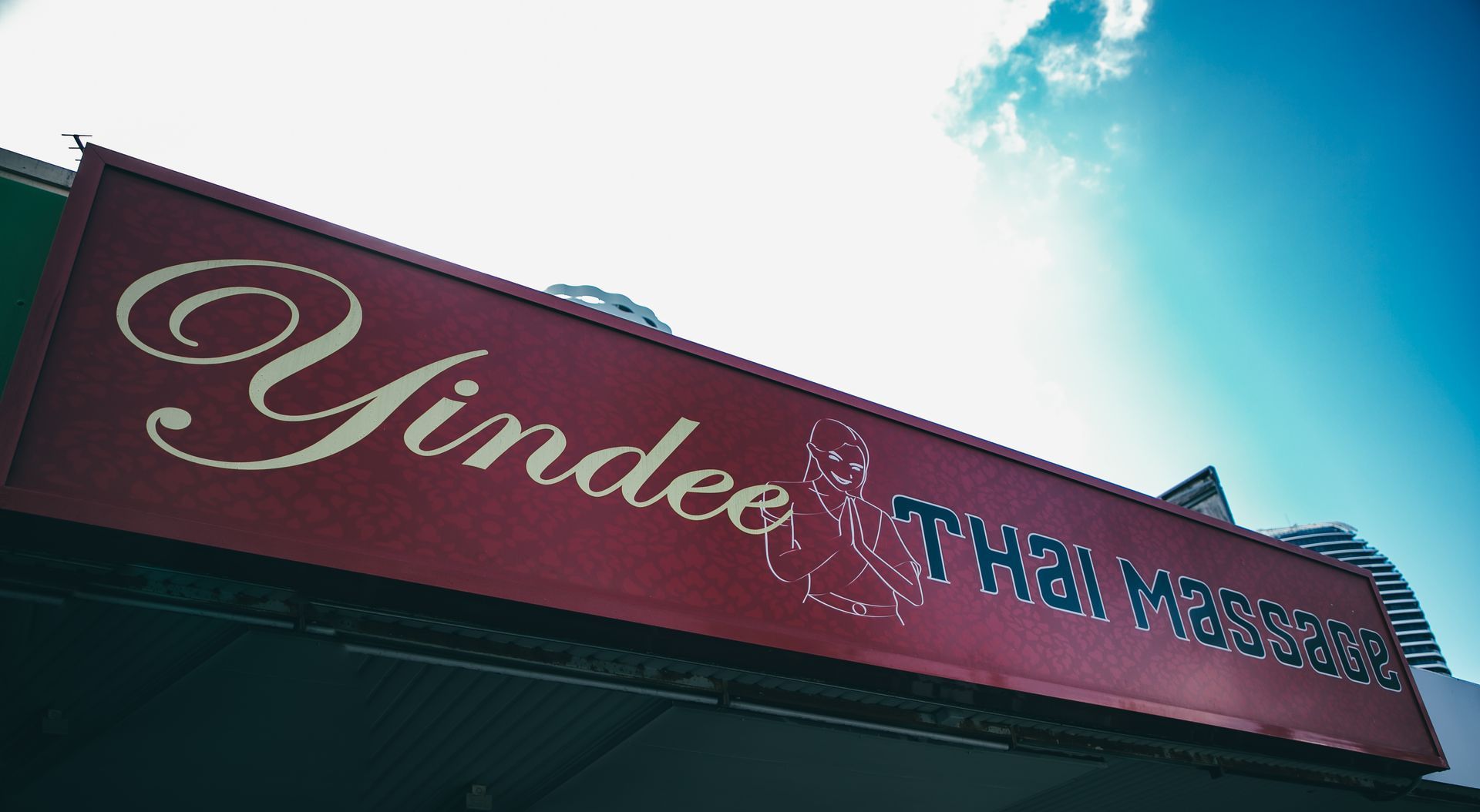 Sign for Yindee Thai Massage in red with white and blue lettering against a blue sky.