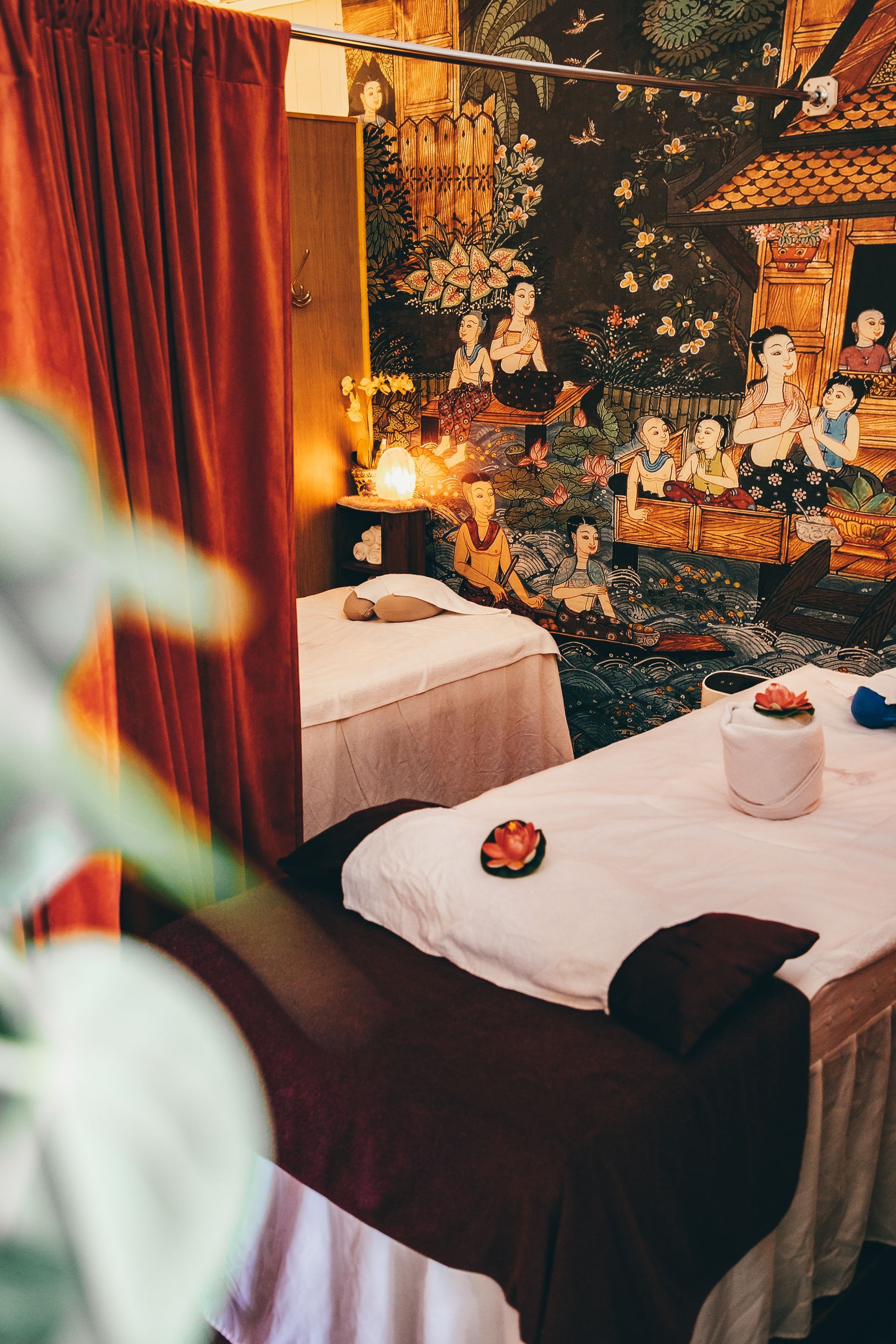 Two massage tables in a spa-like room, red curtain, floral tapestry on wall.
