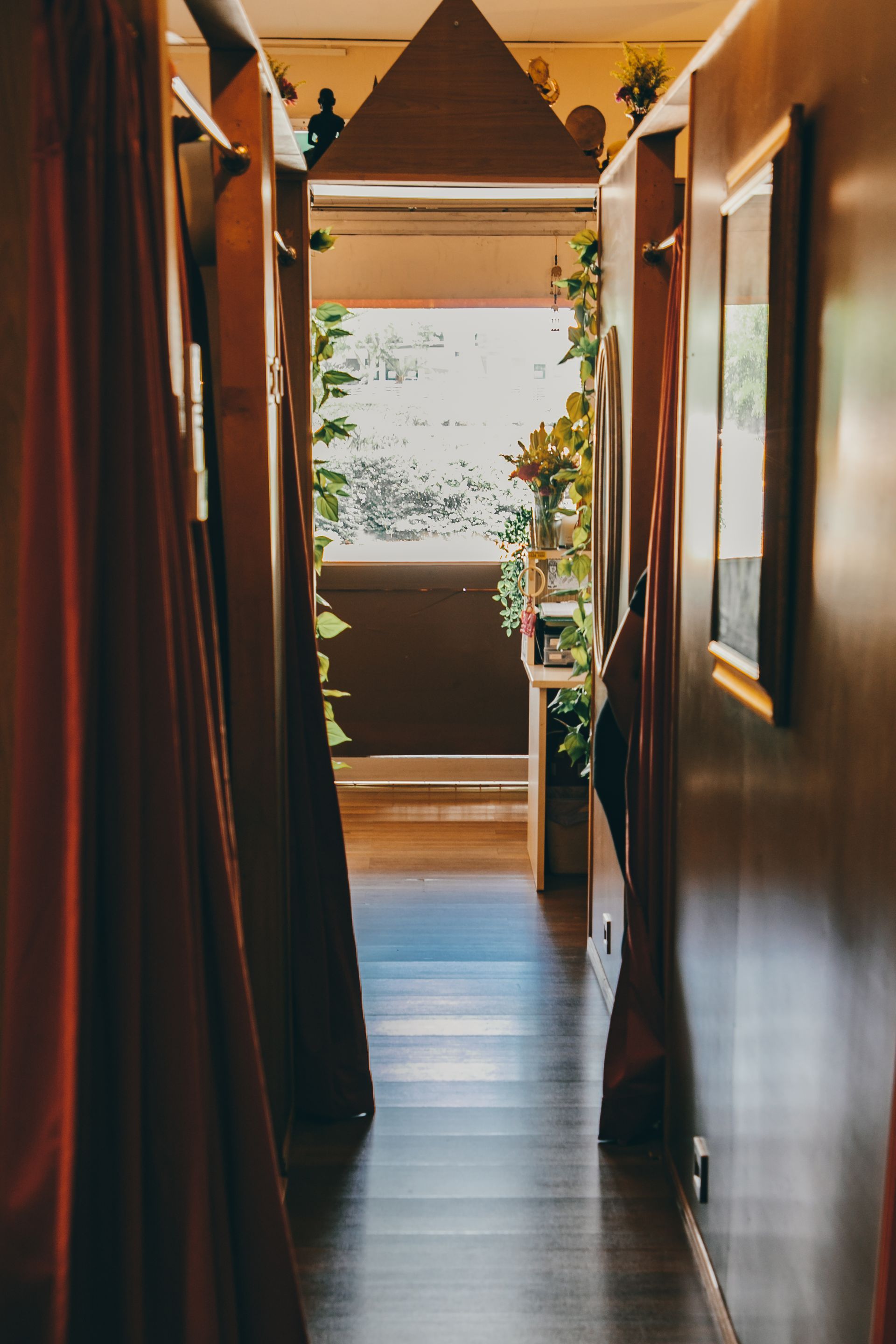 Narrow hallway with dark wood and red curtains, leading to a balcony with greenery.