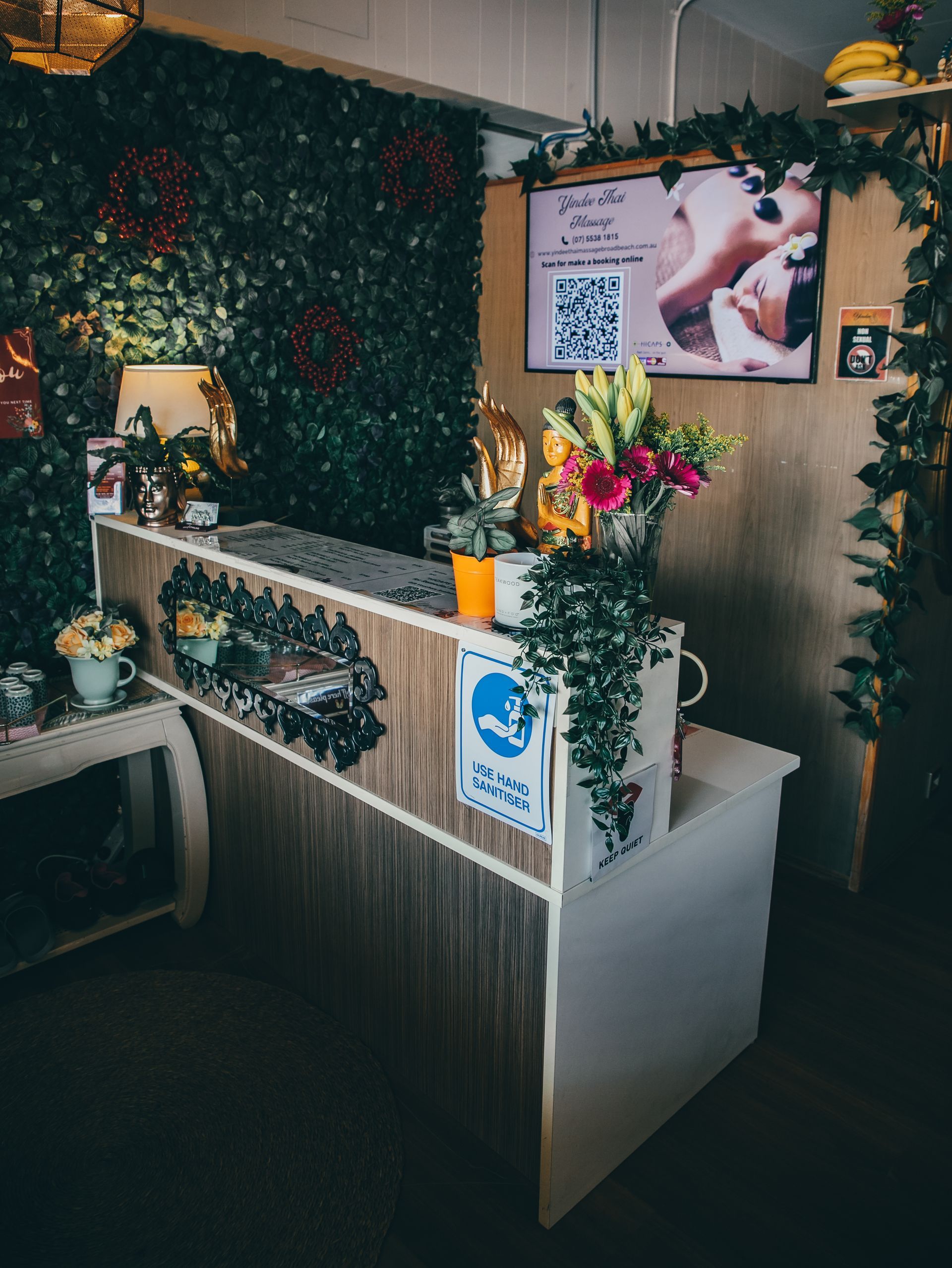 Reception desk with green foliage, flowers, and a sign.
