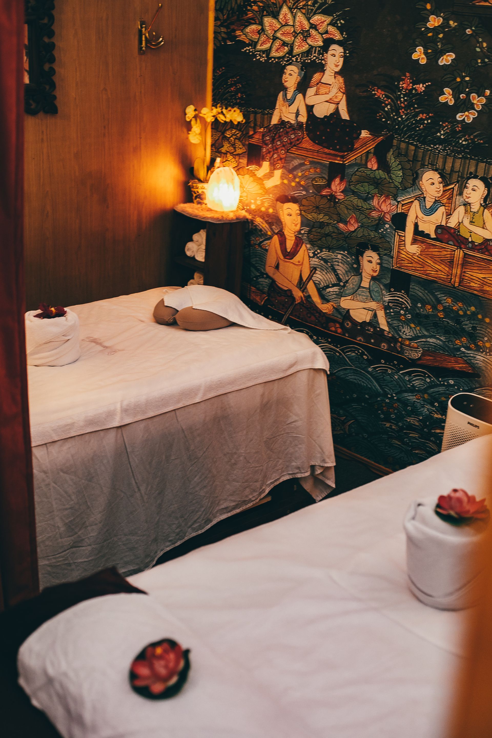 Two massage tables in a dimly lit room with an Asian mural and candles.