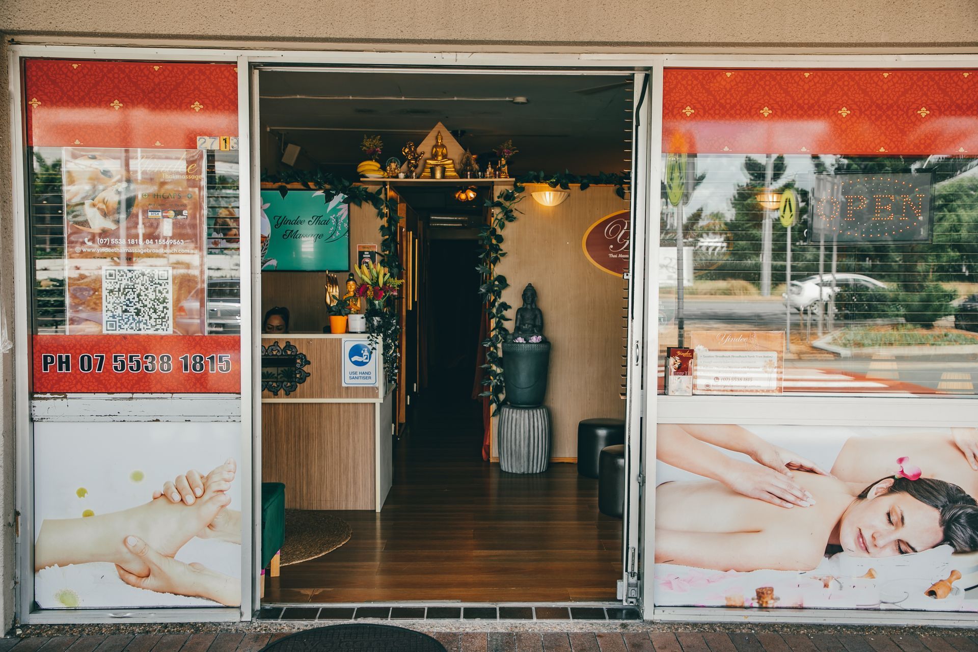 A storefront with glass doors, promoting massage therapy. The interior has a reception desk and a dark hallway.