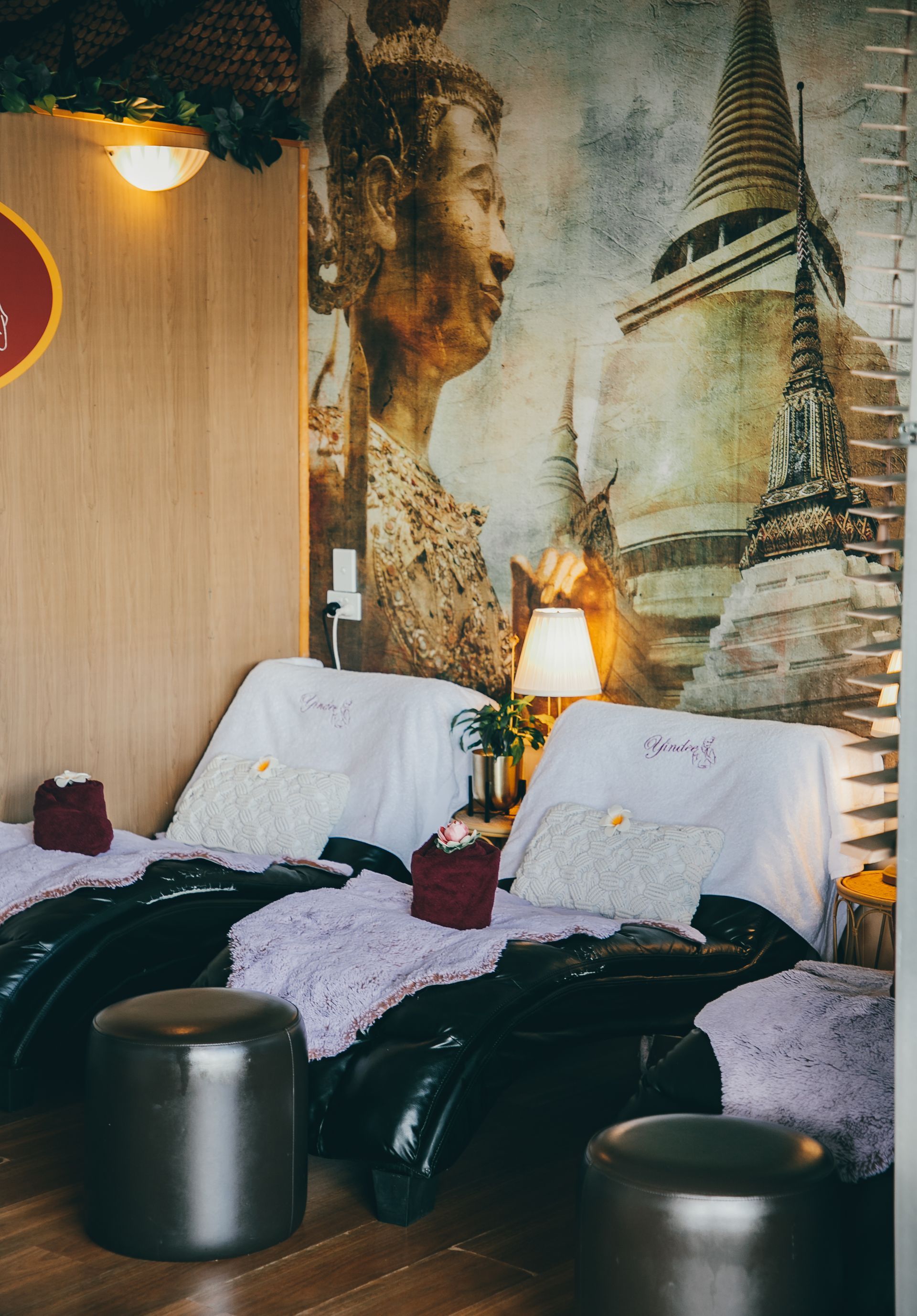 Massage chairs in a spa, with decorative blankets and Buddhist mural in the background.