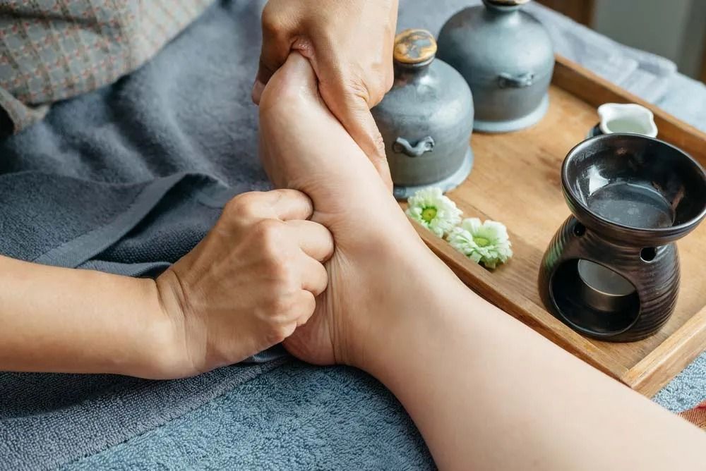 Hands Massaging a Foot in Spa Setting; Essential Oils, Candles, and Flowers — Traditional Massage Services In Broadbeach, QLD