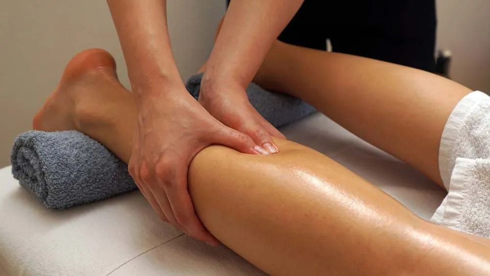 Hands Massaging a Leg on a Massage Table, With a Towel Under the Ankle — Traditional Massage Services In Broadbeach, QLD
