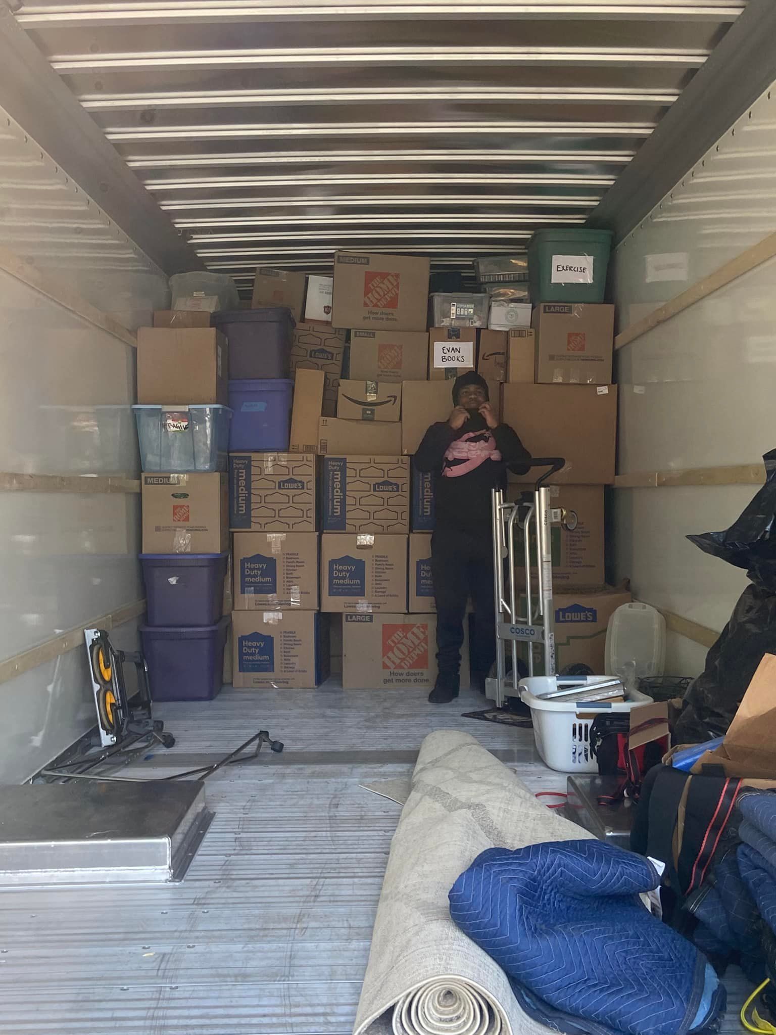 Person standing in a packed moving truck, surrounded by boxes and household items.