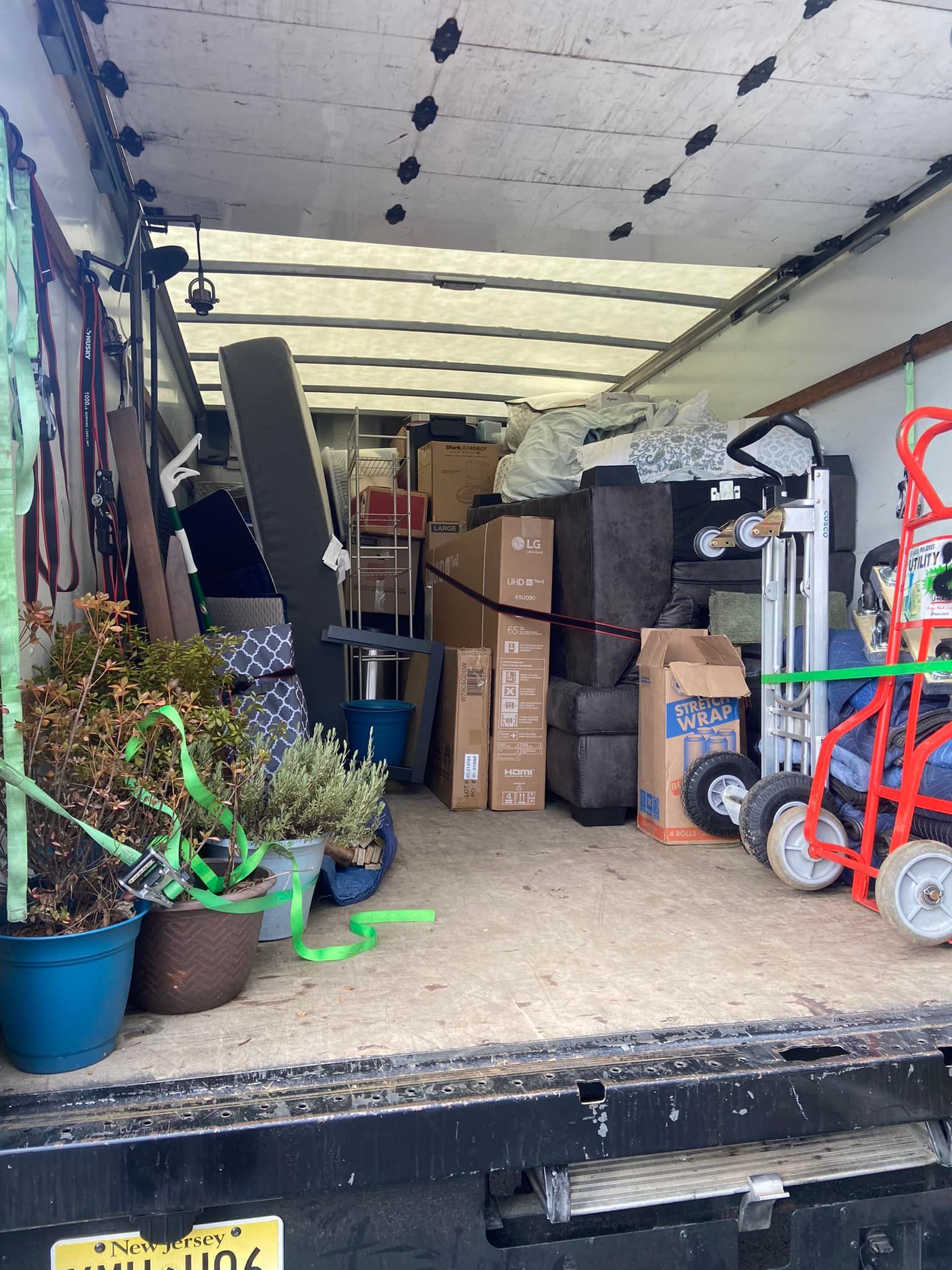 Truck bed loaded with furniture, plants, and boxes for moving.