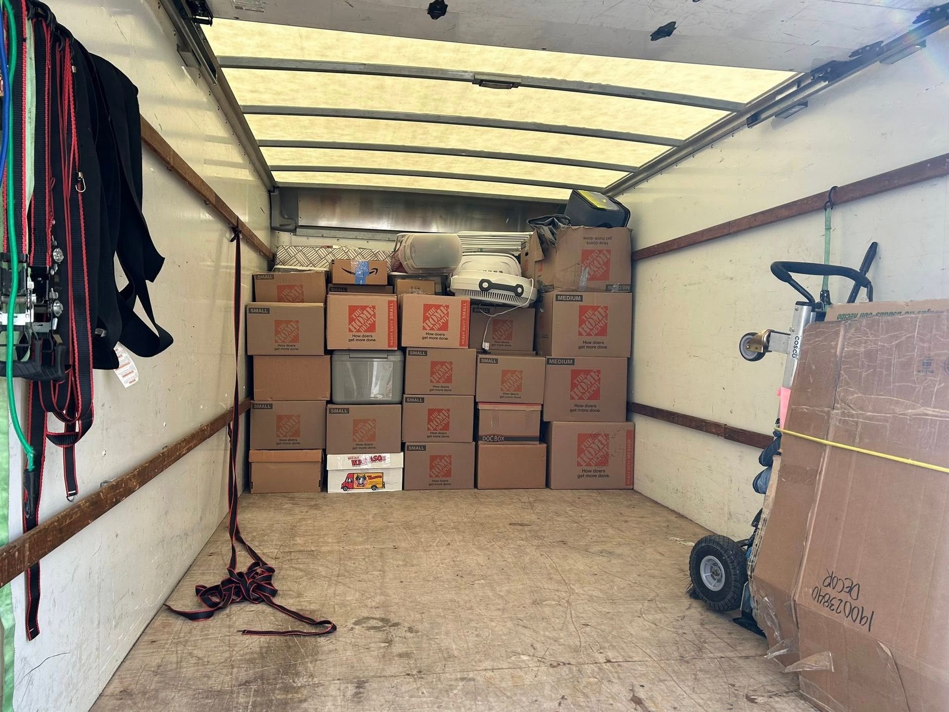 Boxes stacked inside a moving truck with hand truck and hanging items.