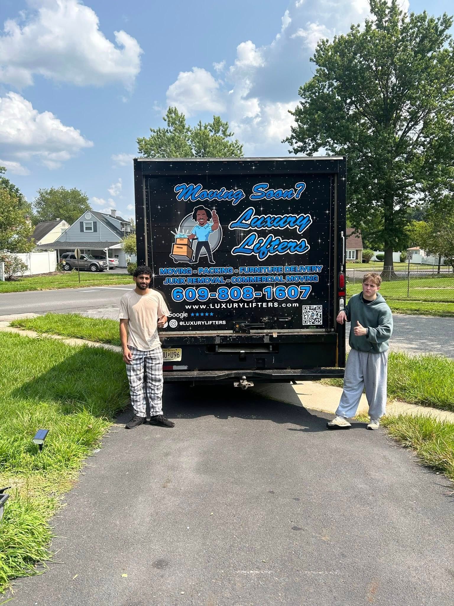Two people standing in front of a moving truck with company logo on the back on a sunny day.