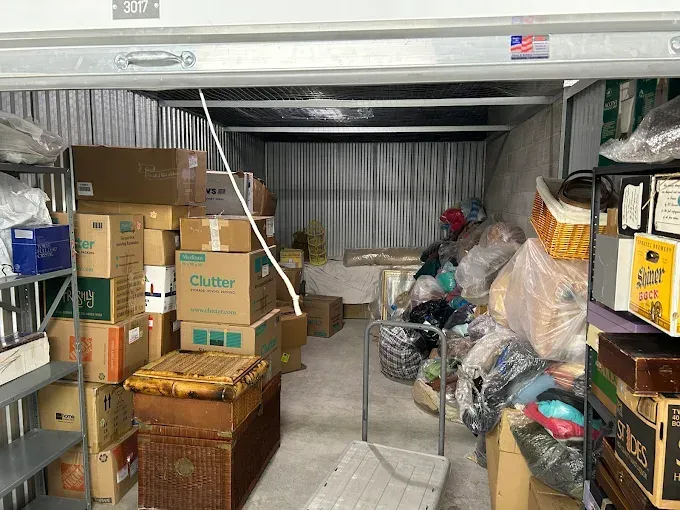 Storage unit filled with boxes, baskets, and bags, some on shelves.
