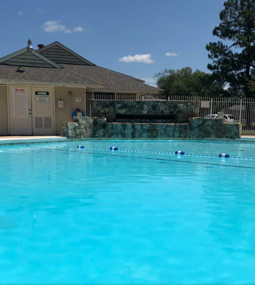 Swimming pool with blue water, small waterfall, and a building under a sunny sky.