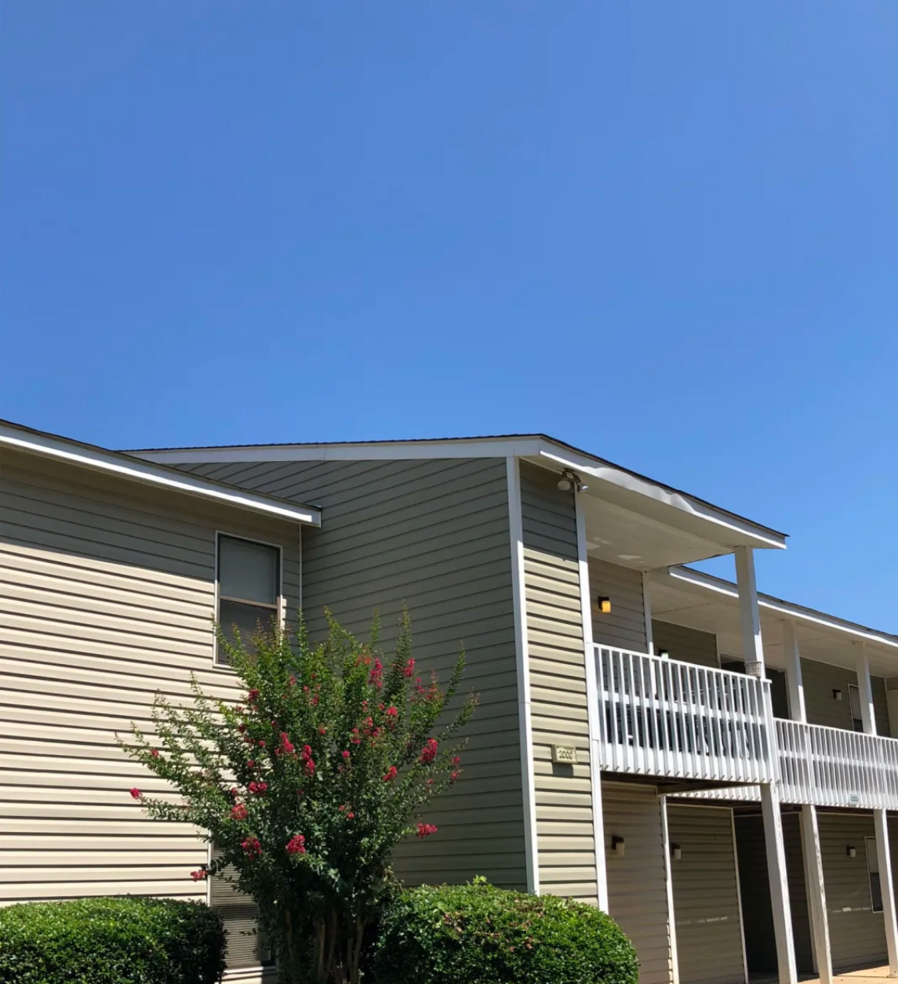 Apartment building with tan siding and white balconies, blue sky.