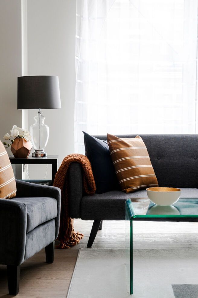 Living room with gray sofa, arm chair, and glass coffee table. Neutral color palette with copper accents.