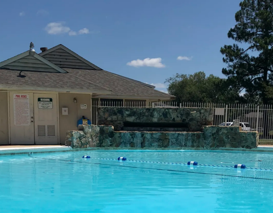 Pool with clear blue water, small building with a waterfall feature, bright blue sky.