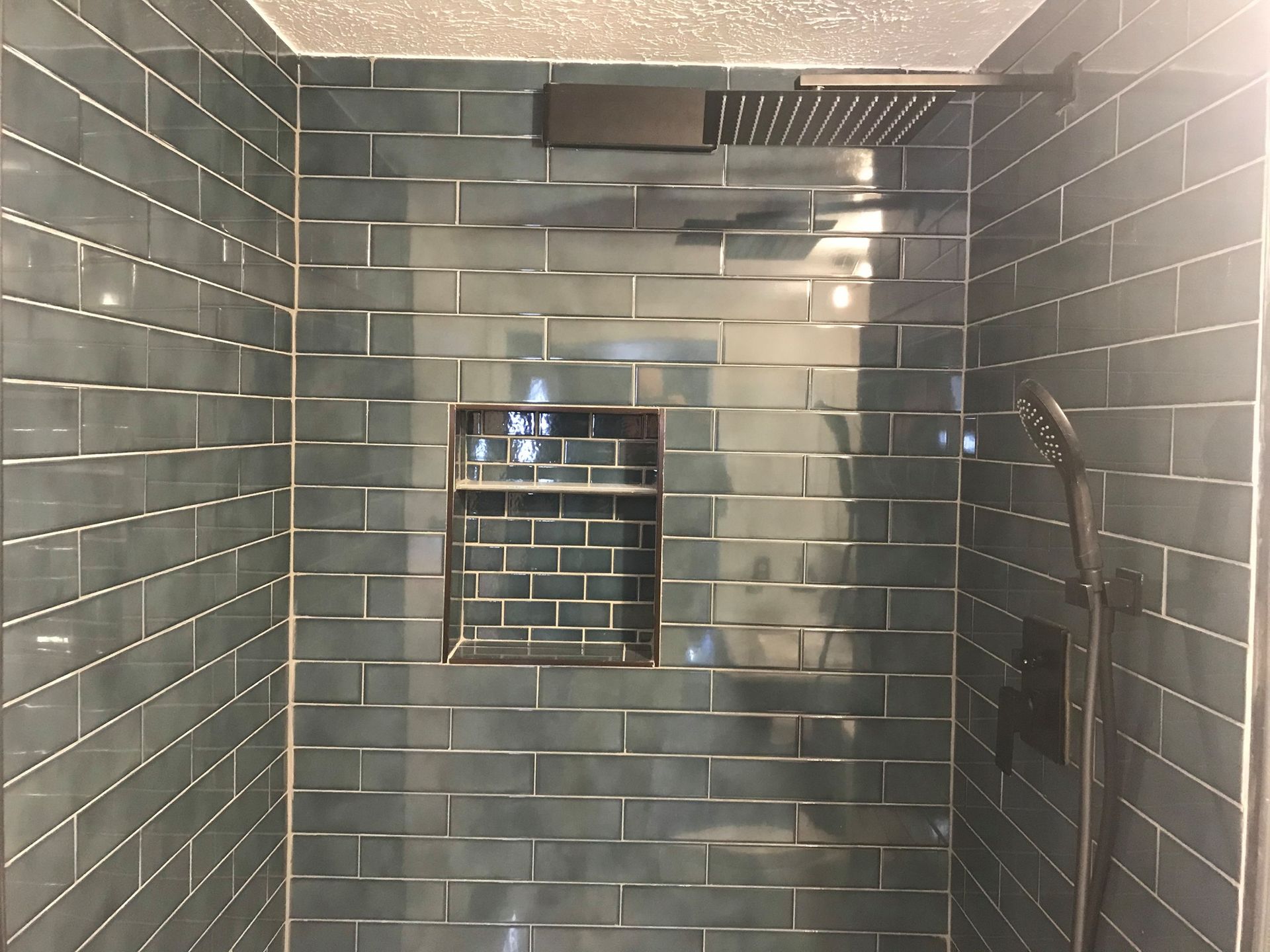 Dark teal tiled shower with a recessed shelf and rain shower head.