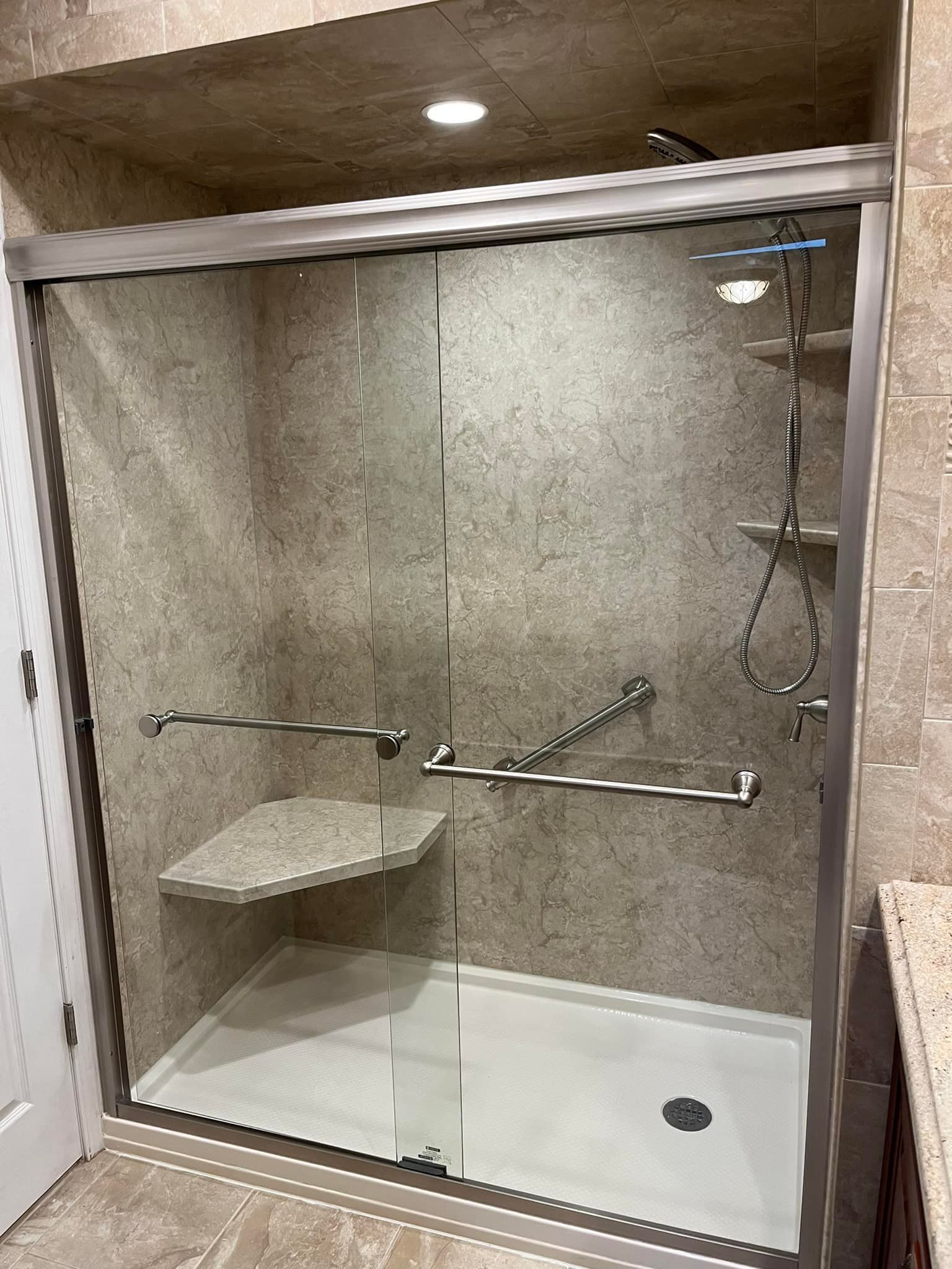 Accessible shower with grab bars, built-in seat, and sliding glass door. Beige walls.