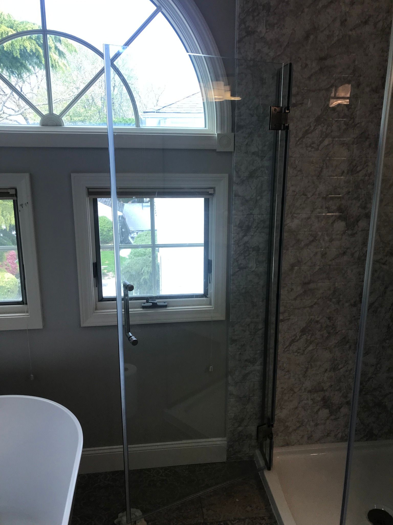 Shower enclosure with glass door next to window with white trim.