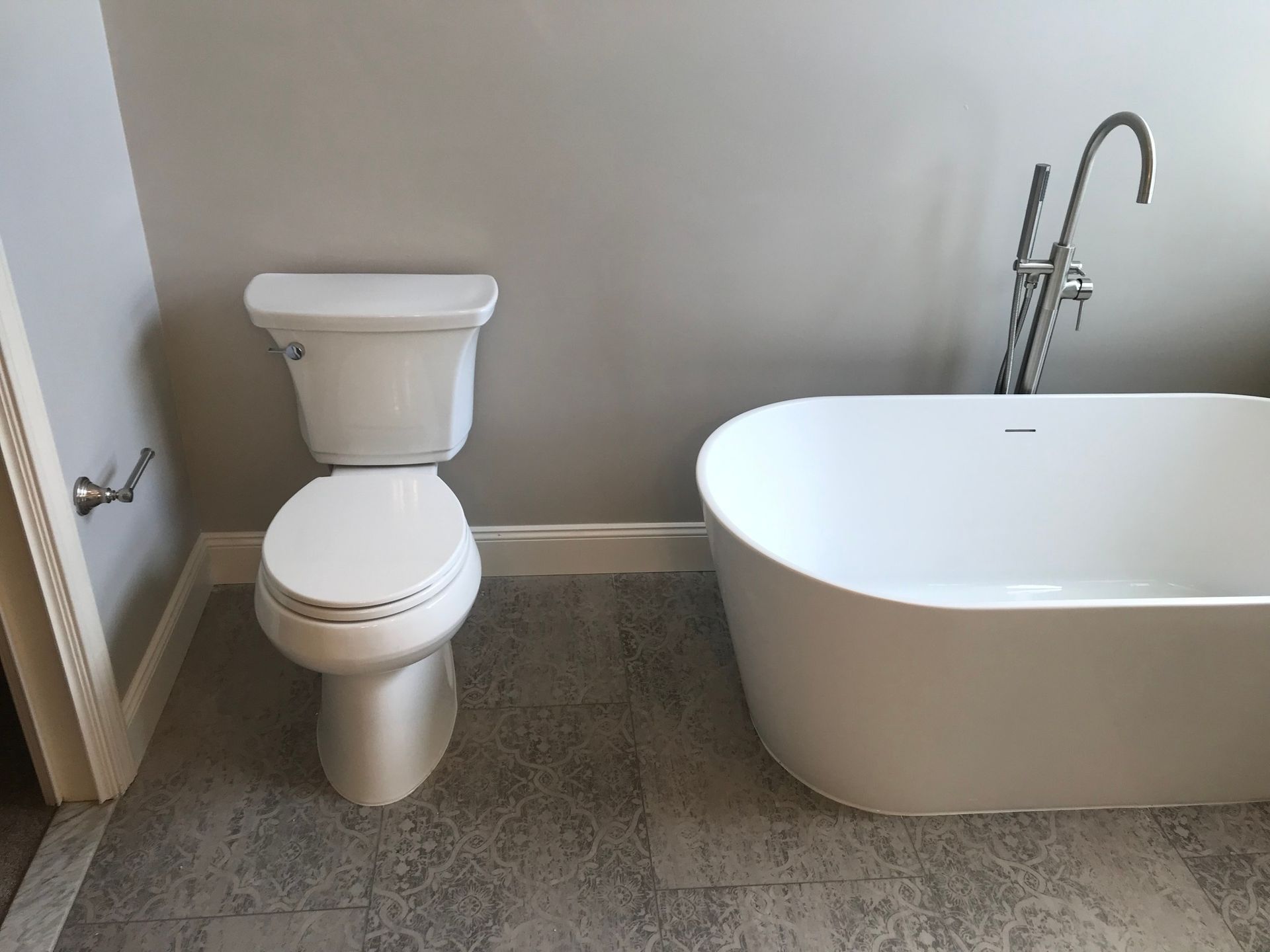 A modern bathroom with a white toilet and a freestanding bathtub on gray tiled floor.