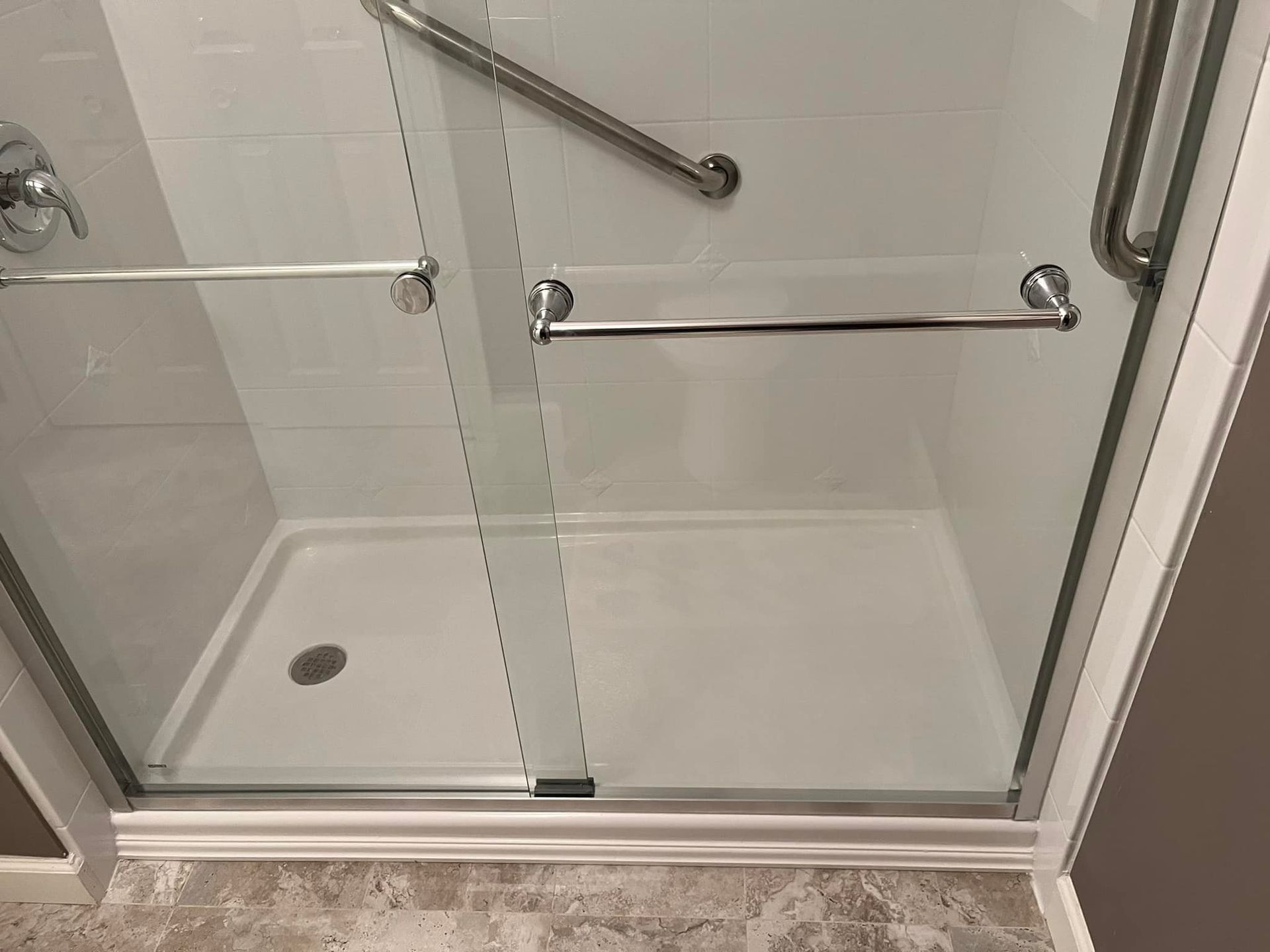 A white shower stall with glass doors, grab bars, and a low threshold.