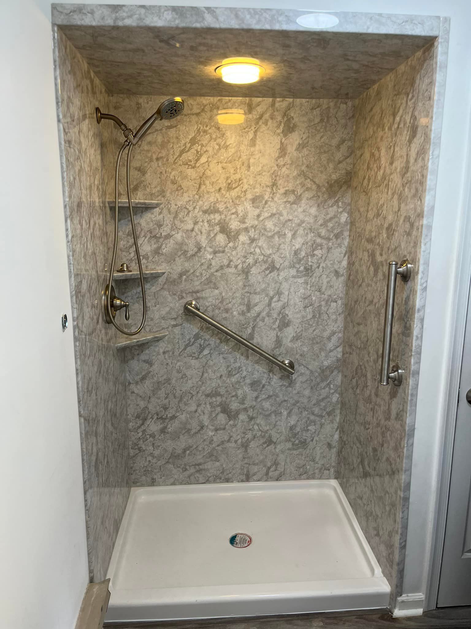 Accessible shower with grab bars, corner shelves, and showerhead. Gray-patterned walls and white base.