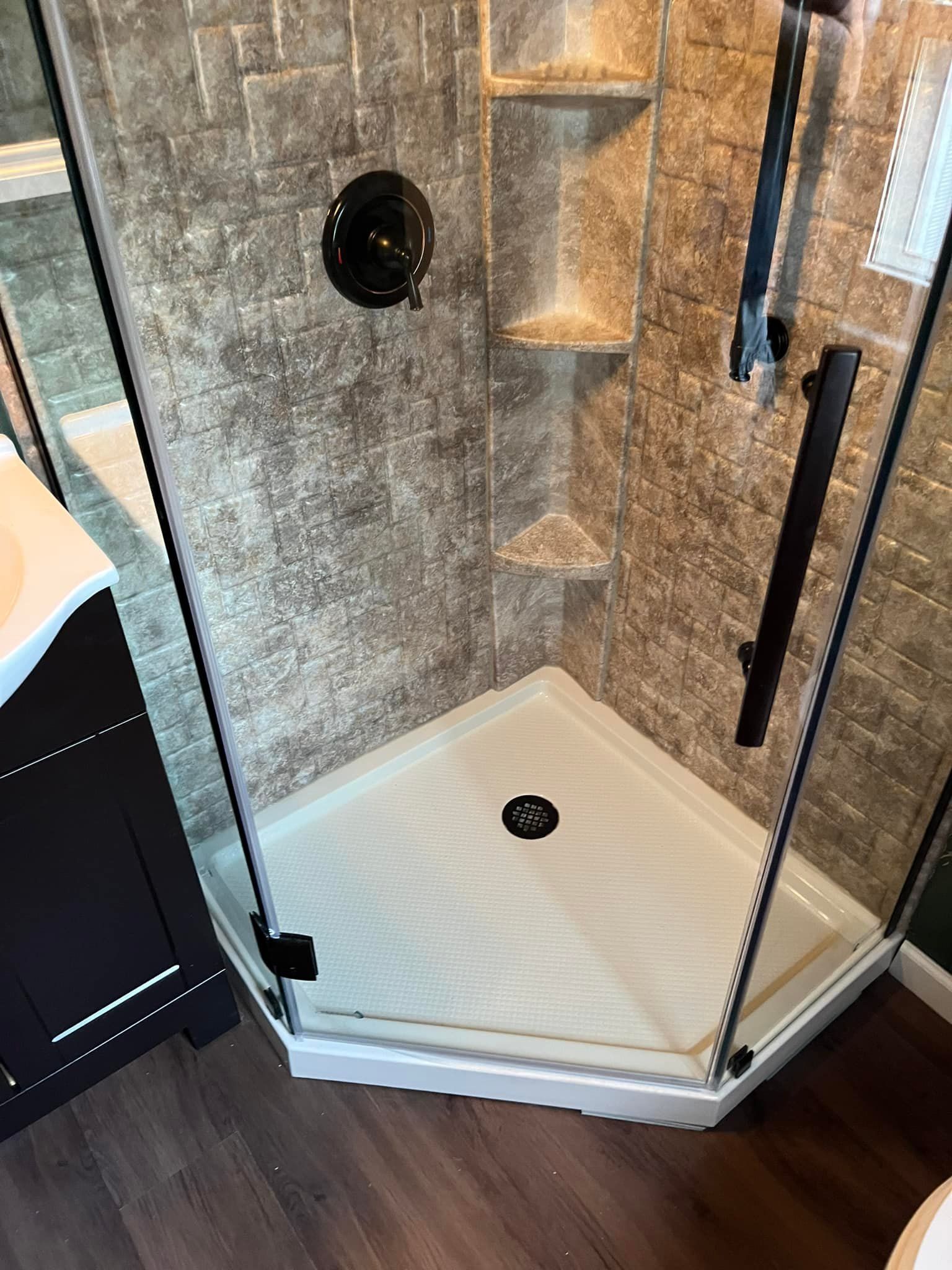Corner shower with glass doors, brown tile walls, and a white base. Black fixtures.