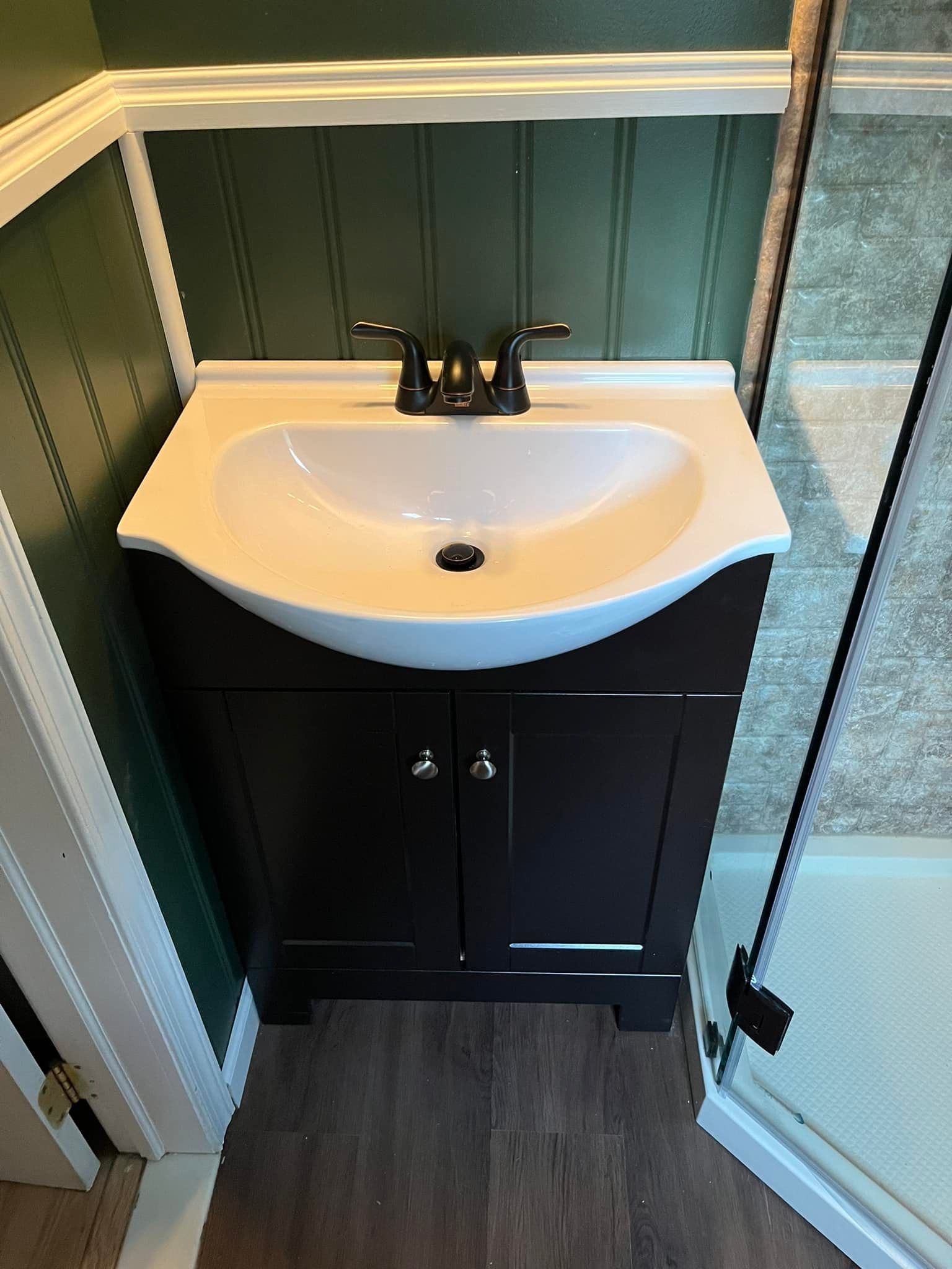 Bathroom vanity with dark brown cabinet, white sink, and black faucet against green paneling.