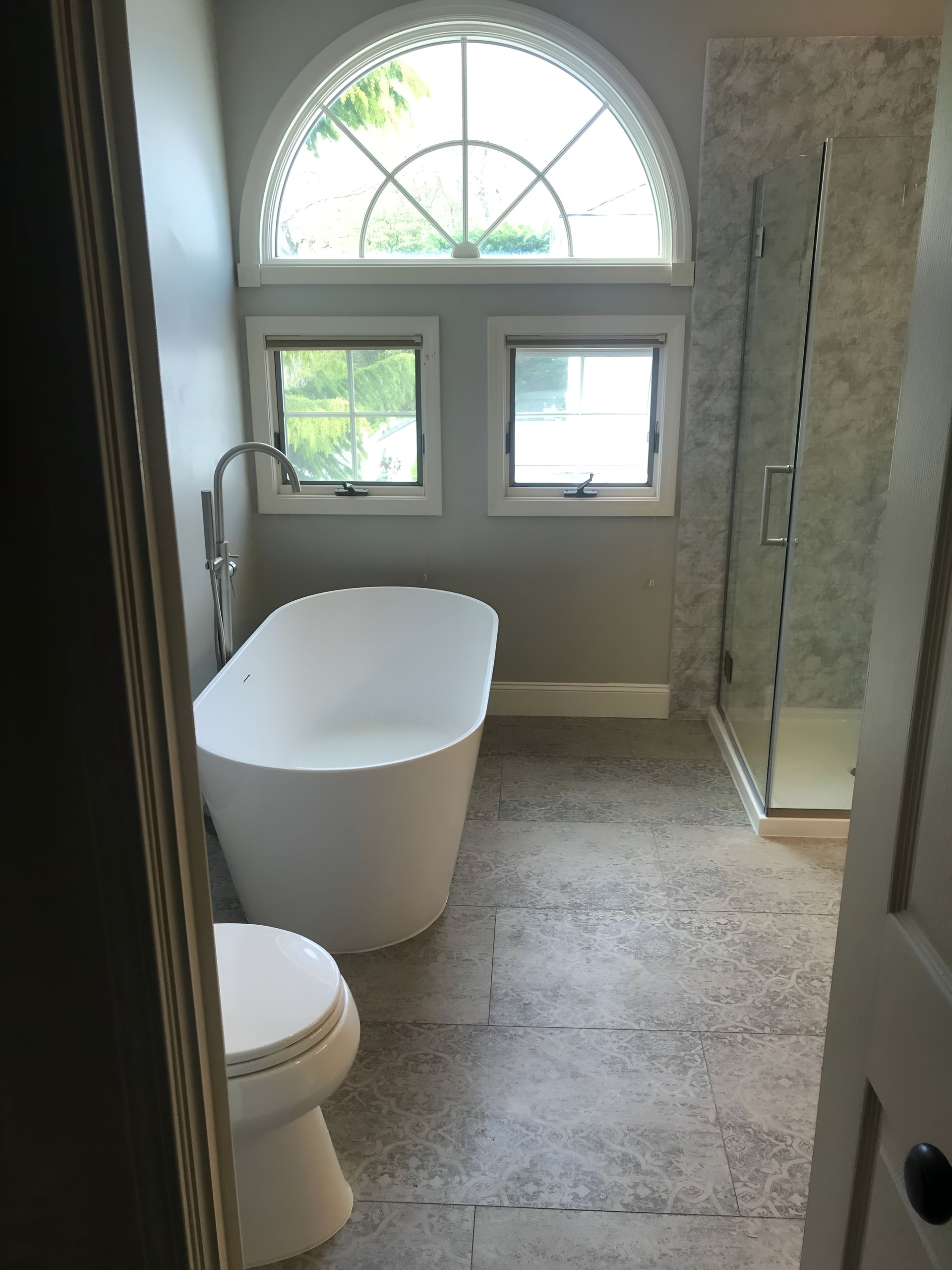 Small bathroom with tub, toilet, and vanity. Beige tiles, light-pink walls, and a small window.