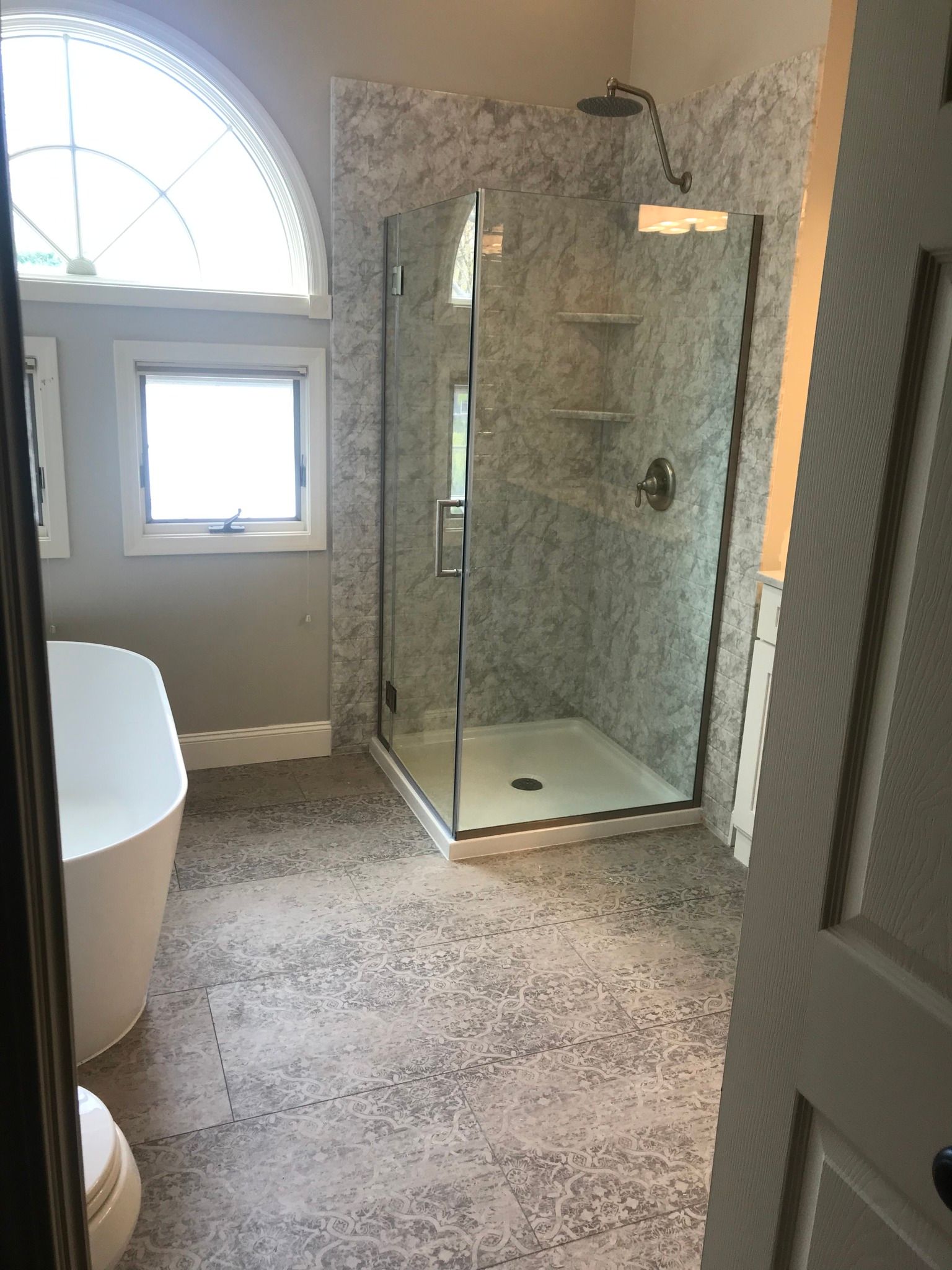 Bathroom with walk-in shower, freestanding tub, tiled walls/floor, and arched window.