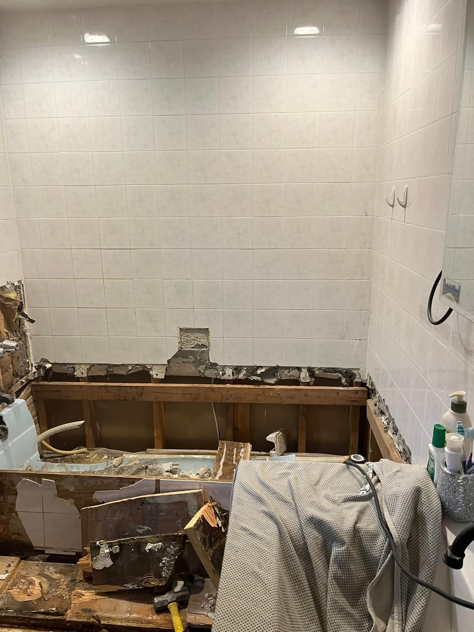 Bathroom renovation in progress; exposed wood, tiled walls, debris, and a partial tub.