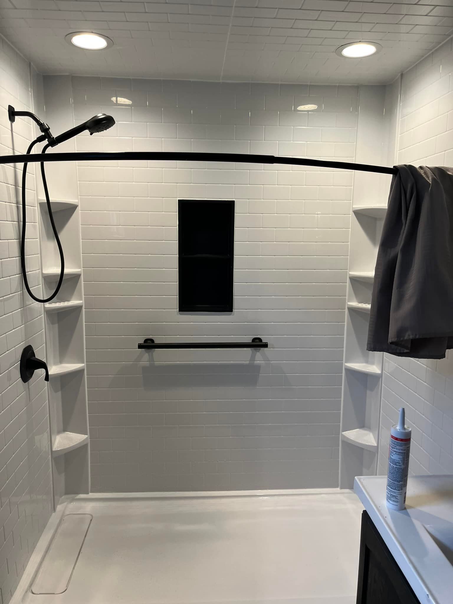 White shower with black fixtures, built-in shelves, and a grab bar; a towel hangs on a rod.