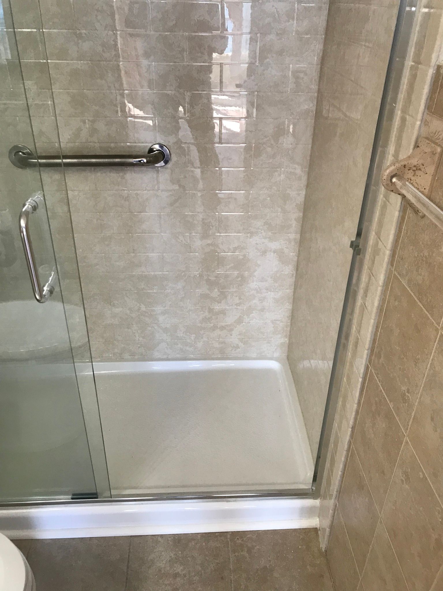 Shower stall with glass door and grab bar. Beige tile walls and white shower pan.