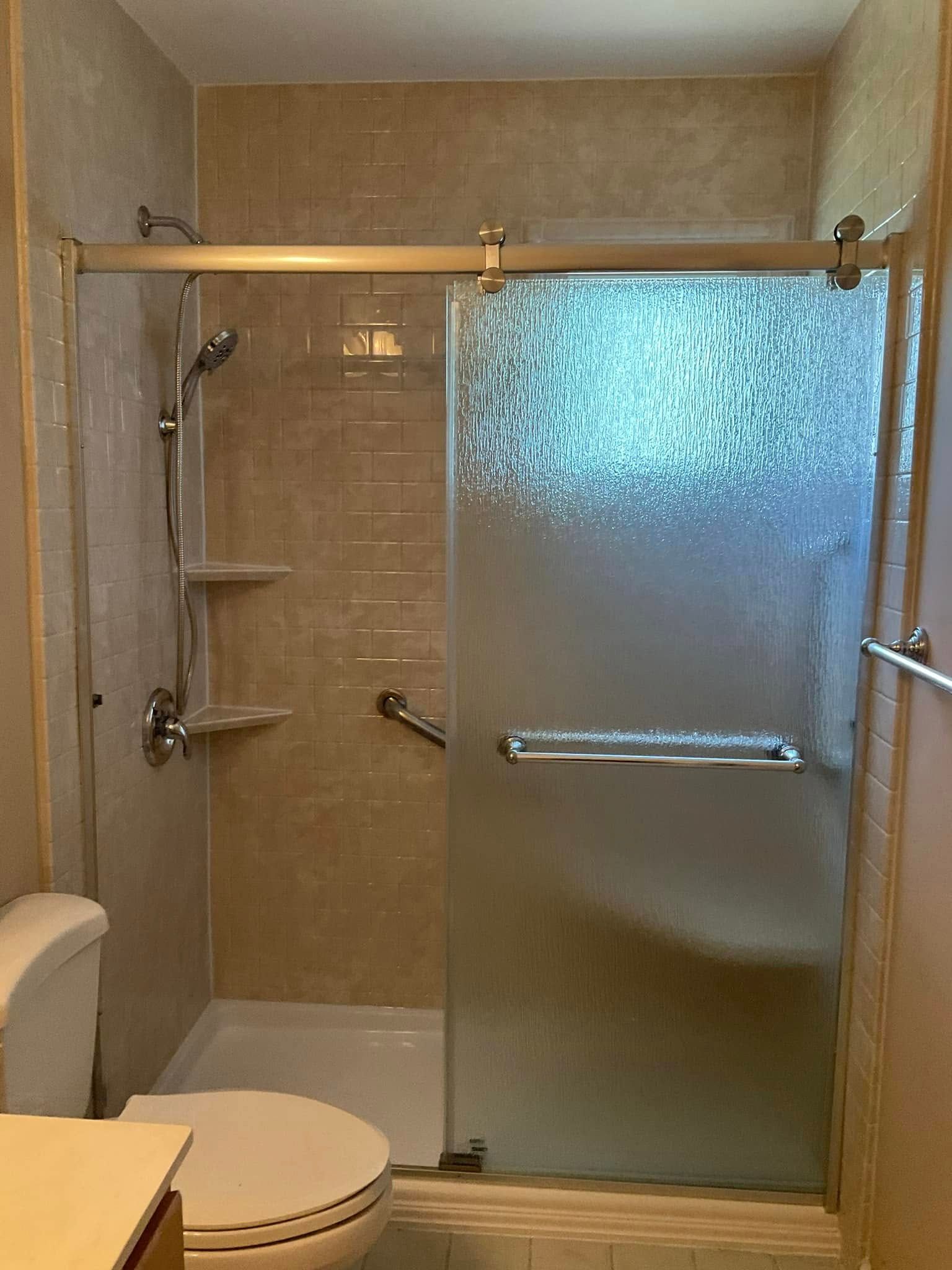 Bathroom with tan tile, sliding glass shower door, toilet, and grab bar.