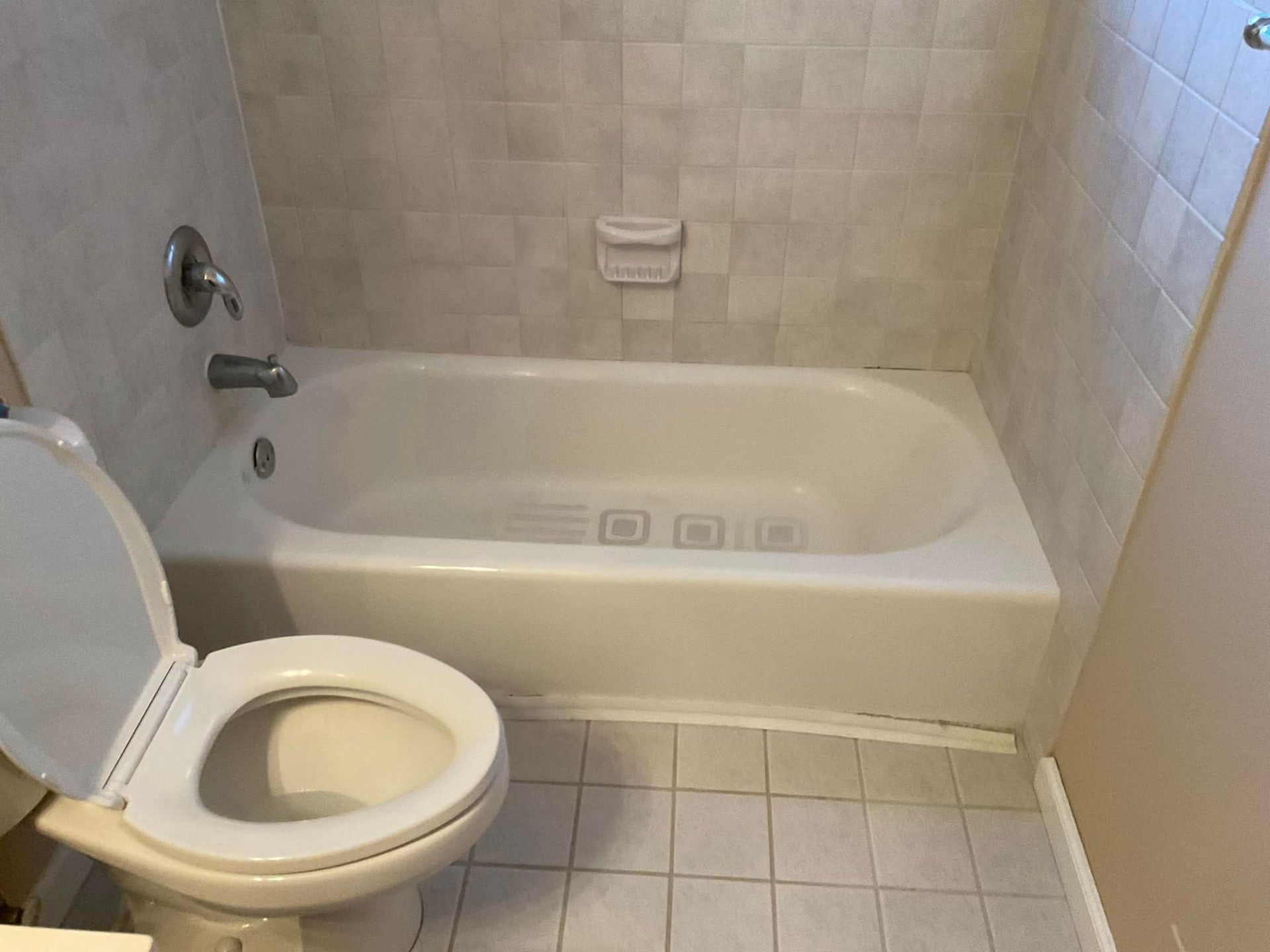 Bathroom with white tub, toilet, and light tile walls.