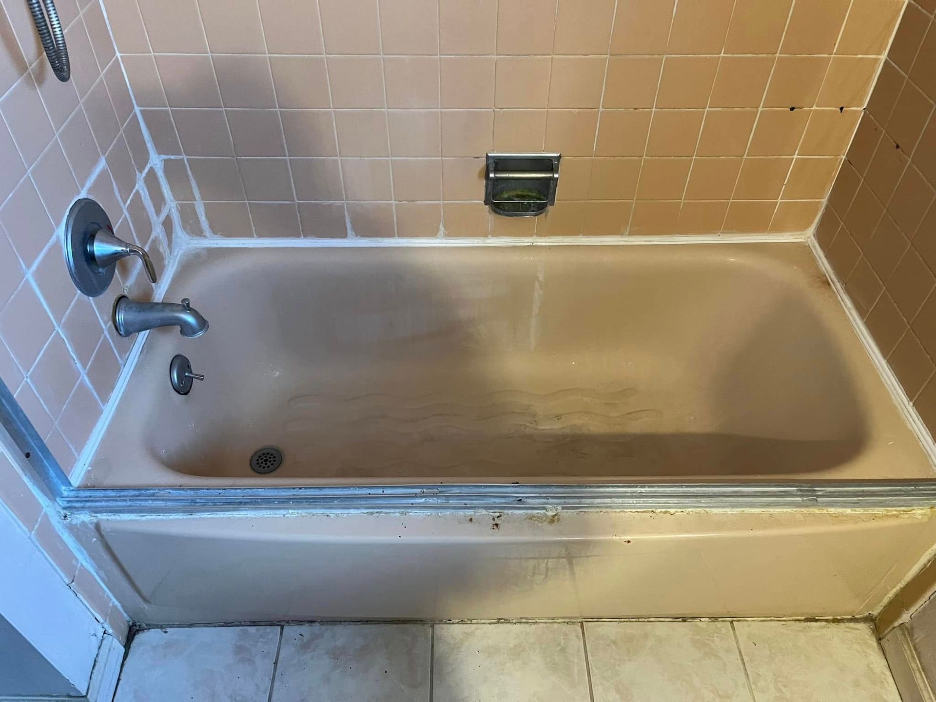 Pink-toned bathtub surrounded by matching tile. Silver fixtures. Grey grout and a partially opened shower door.