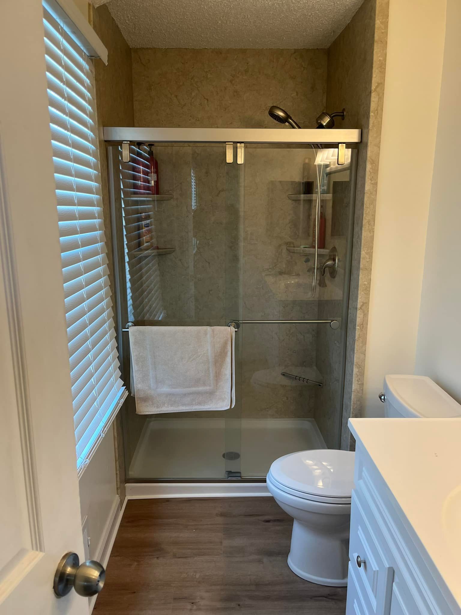 Bathroom with a shower, toilet, and a partially visible window with blinds.