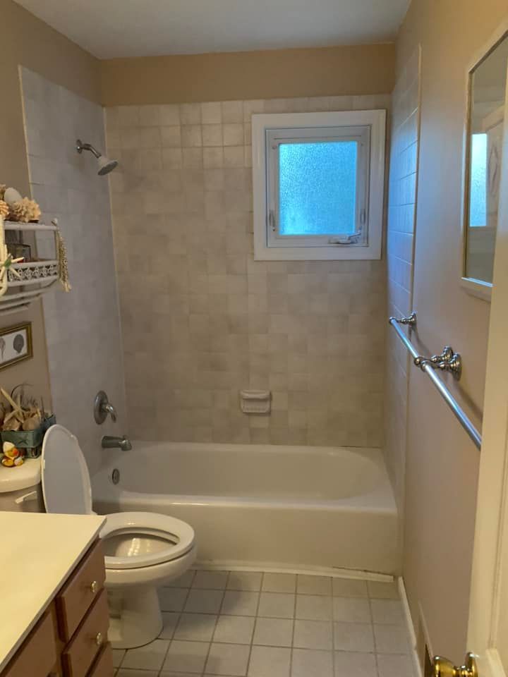 Small bathroom with tub, toilet, and vanity. Beige tiles, light-pink walls, and a small window.