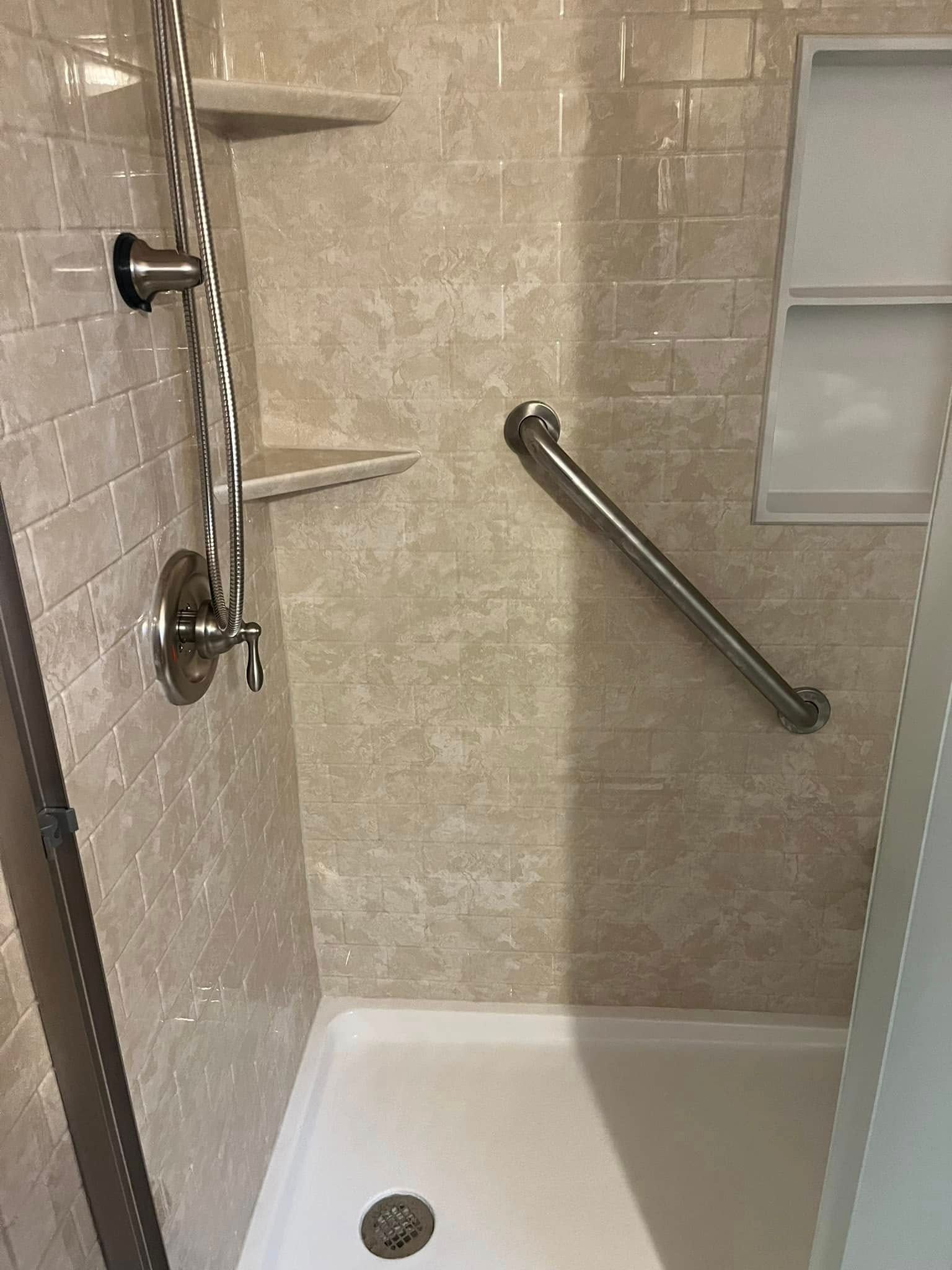 Accessible shower with grab bar, shelves, and neutral-toned tile.