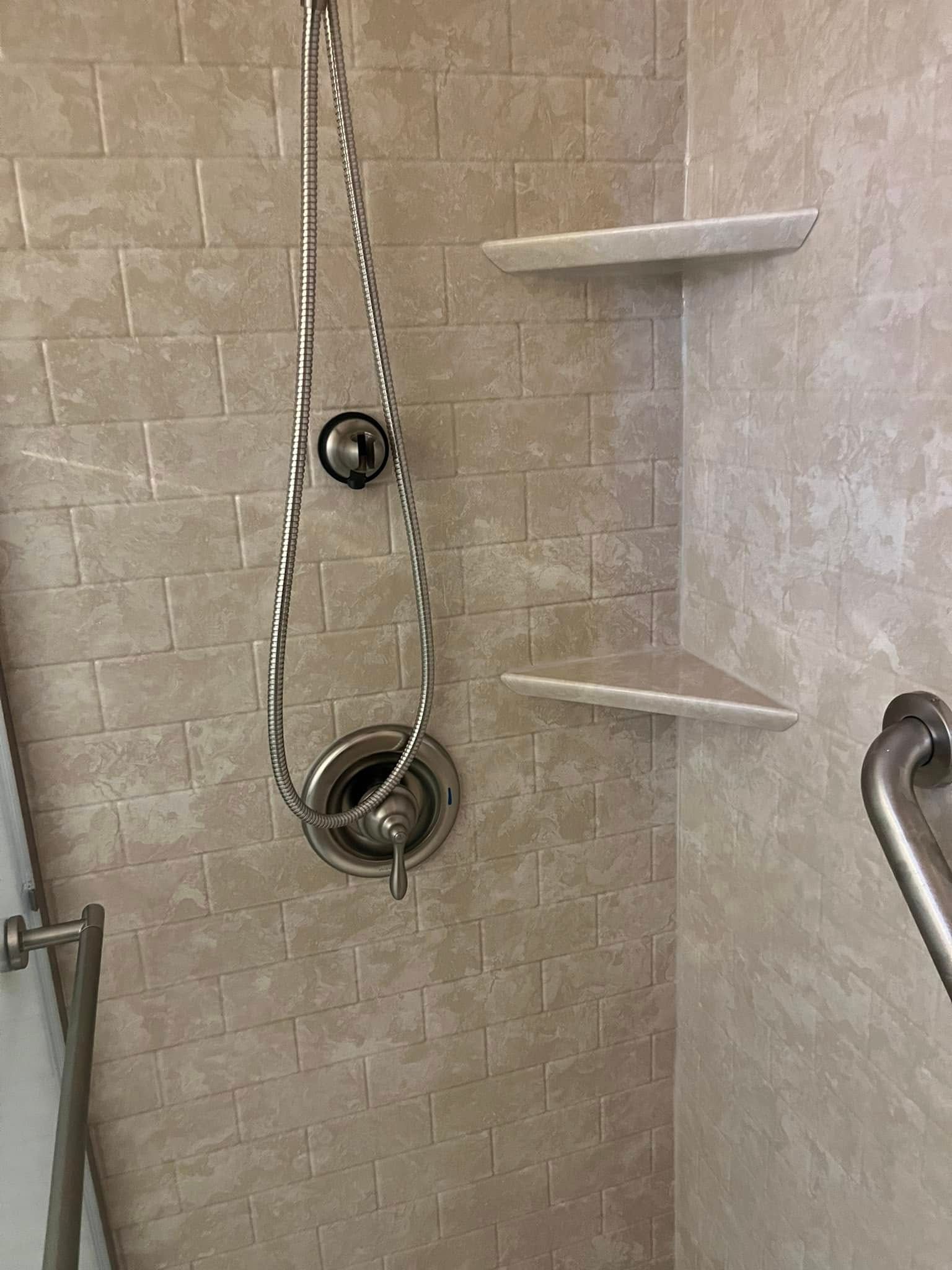 Shower stall with a silver faucet, shelves, and grab bar. Beige tiles.