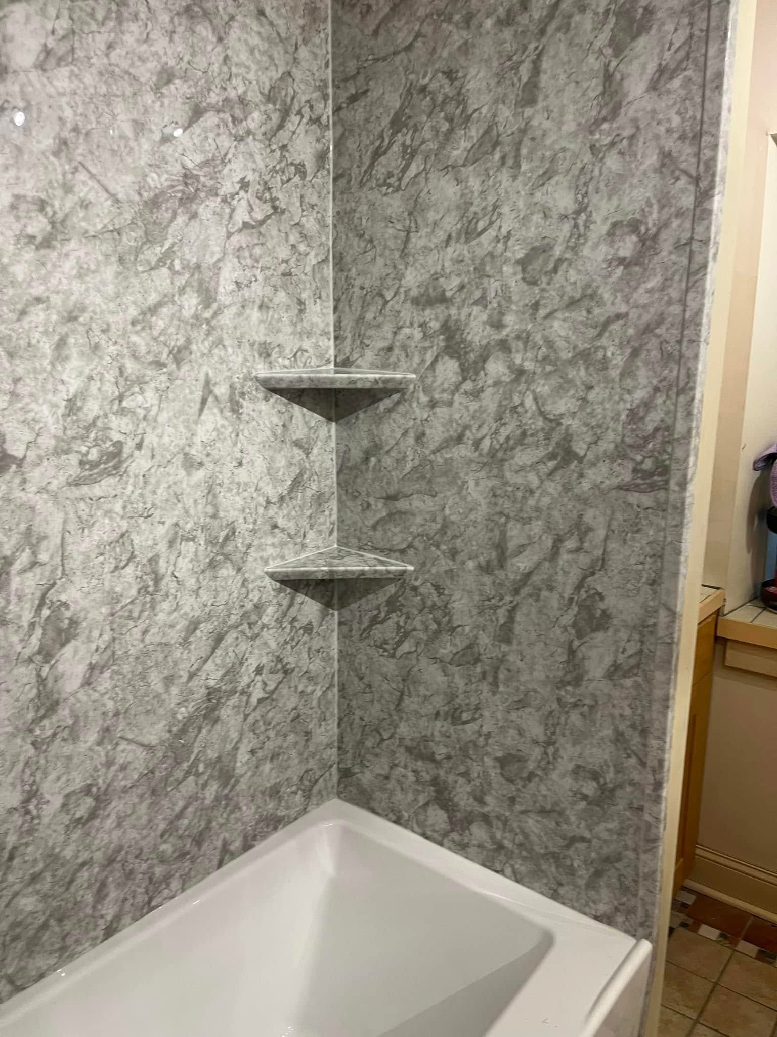 Gray shower surround with two built-in shelves, over a white bathtub.