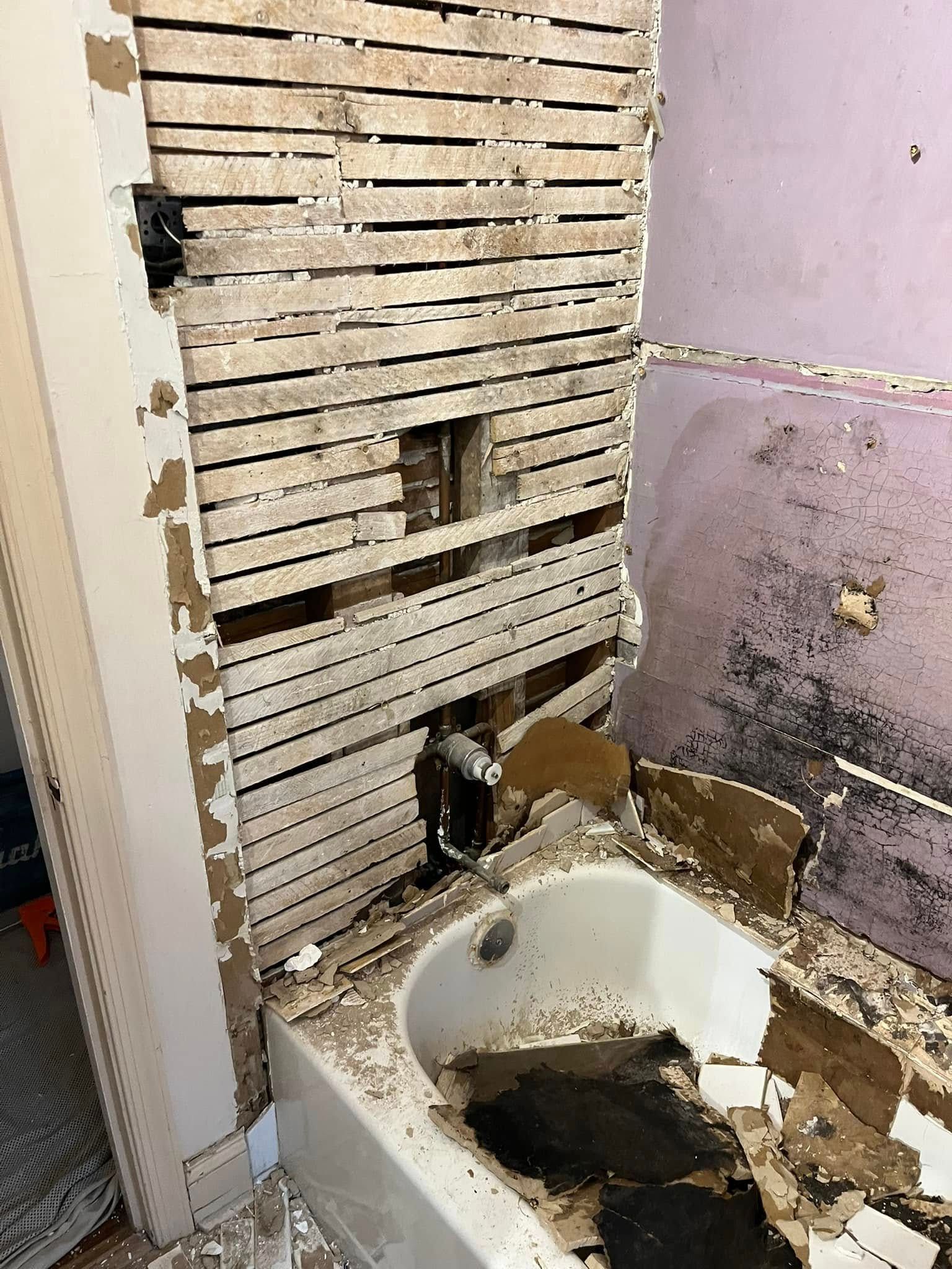 Bathroom in disrepair, exposed studs, damaged wall, bathtub, and possible mold.