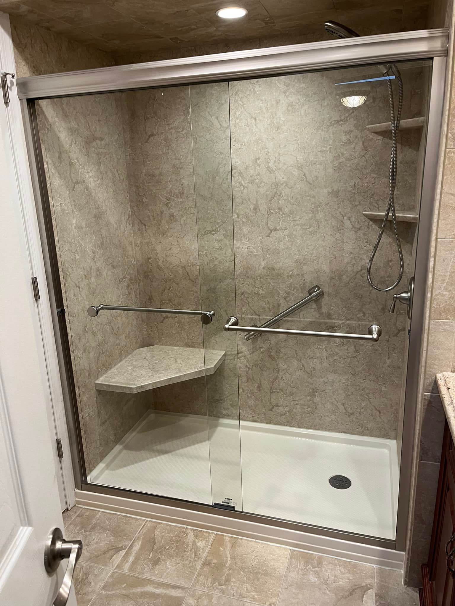 Accessible shower with a built-in seat, grab bars, and a sliding glass door. Beige walls and floor.