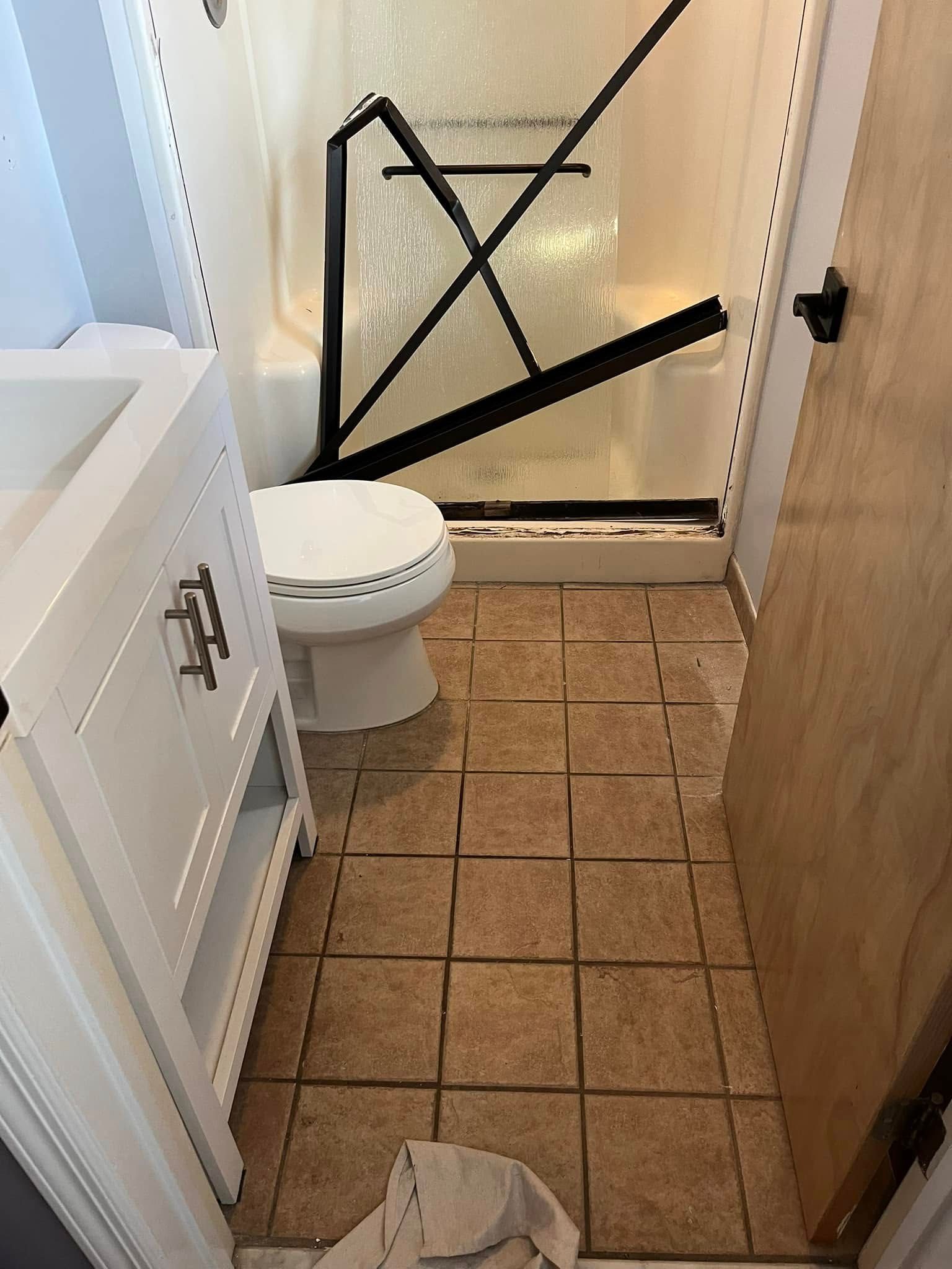 Bathroom with white vanity, toilet, shower, brown floor tiles, and a partially open wooden door.