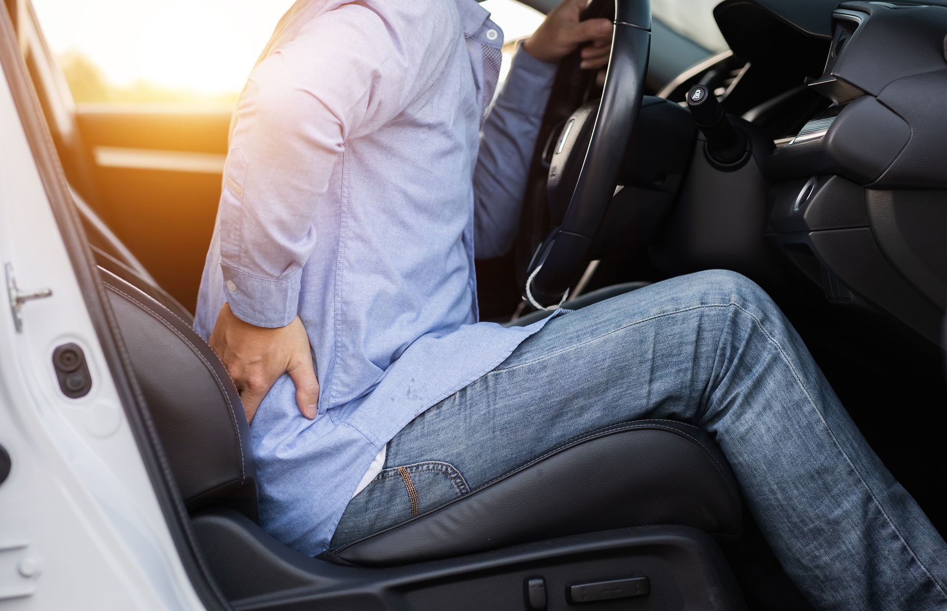 A man is sitting in the driver 's seat of a car holding his back in pain.