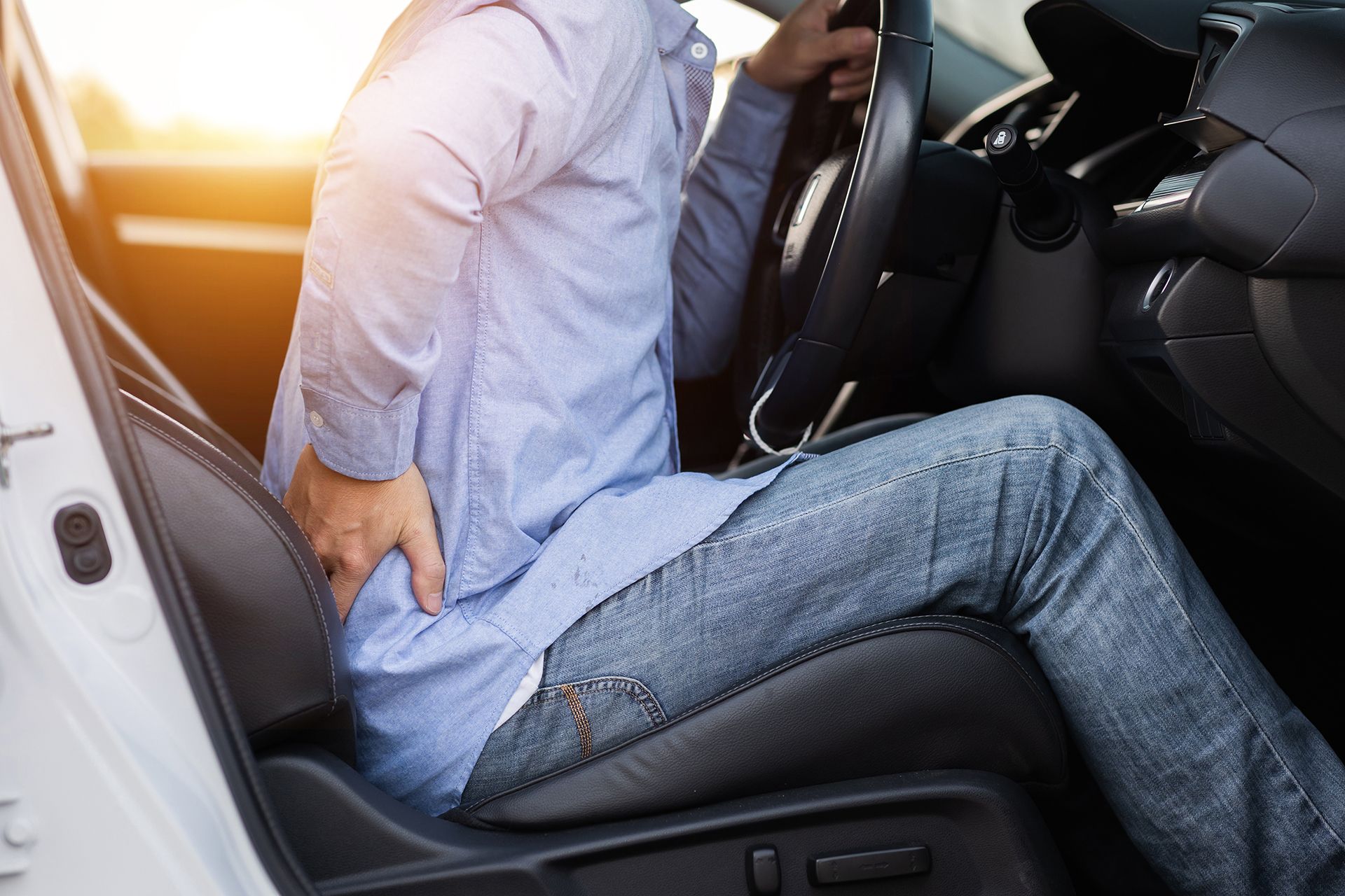 A man is sitting in a car holding his back in pain.