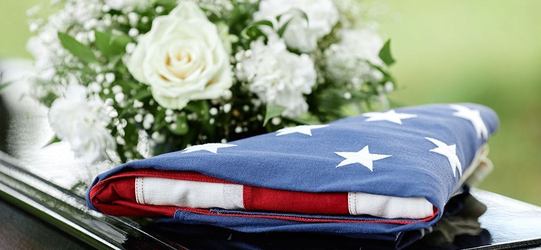 An american flag is laying on top of a limousine next to a bouquet of flowers.