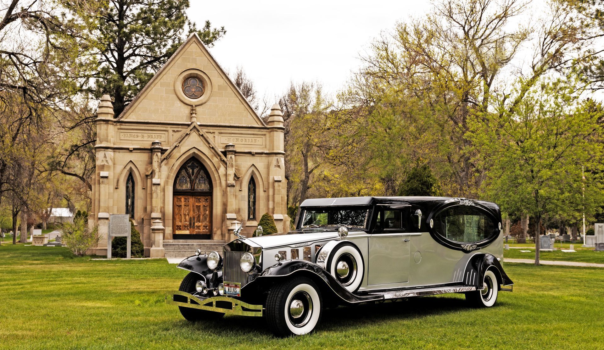 A funeral car is parked in front of a church in a cemetery.