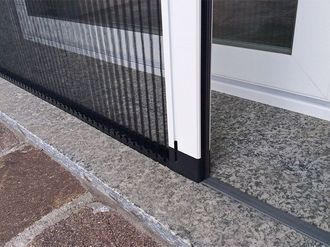 Zanzariera plissettata nera nel telaio della porta, gradini in pietra grigia.