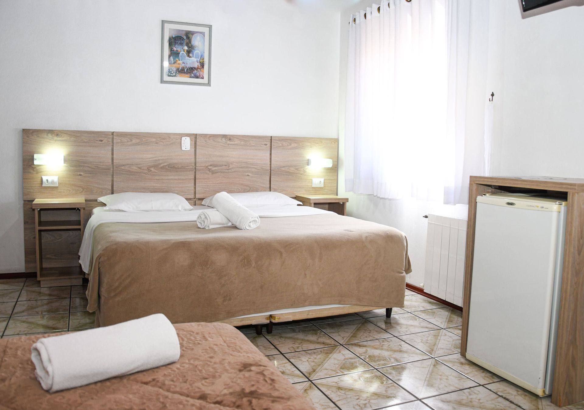 Um quarto de hotel com uma cama grande e uma geladeira pequena.