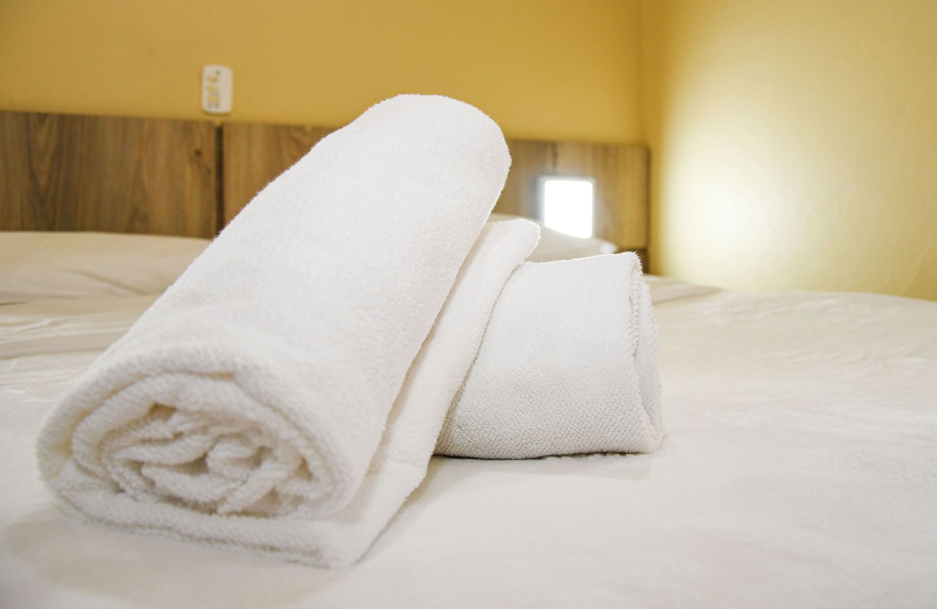 Duas toalhas estão enroladas em uma cama em um quarto de hotel.